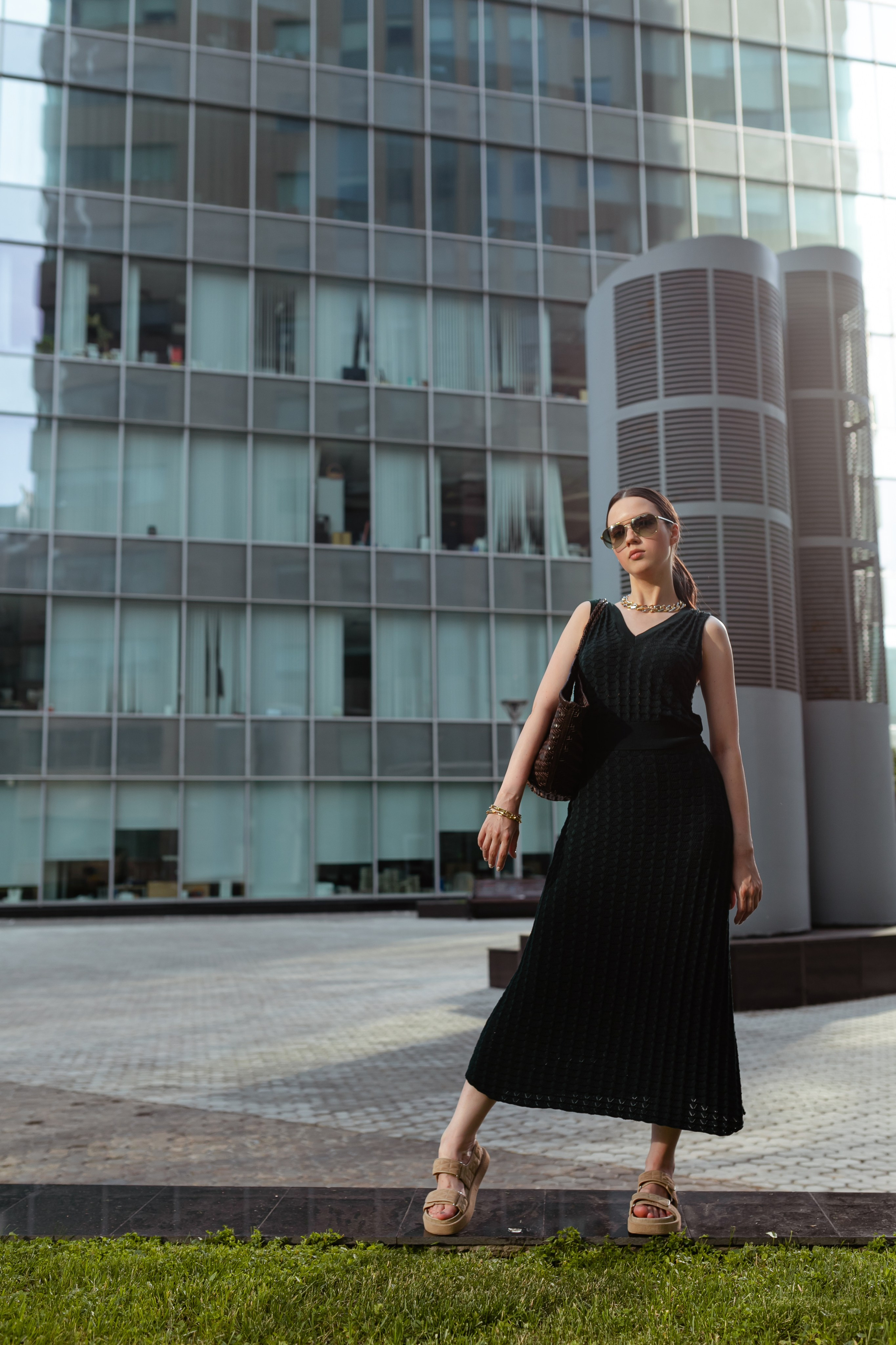 Девушка в стильный одежде позирует фотографу на фоне стеклянного здания