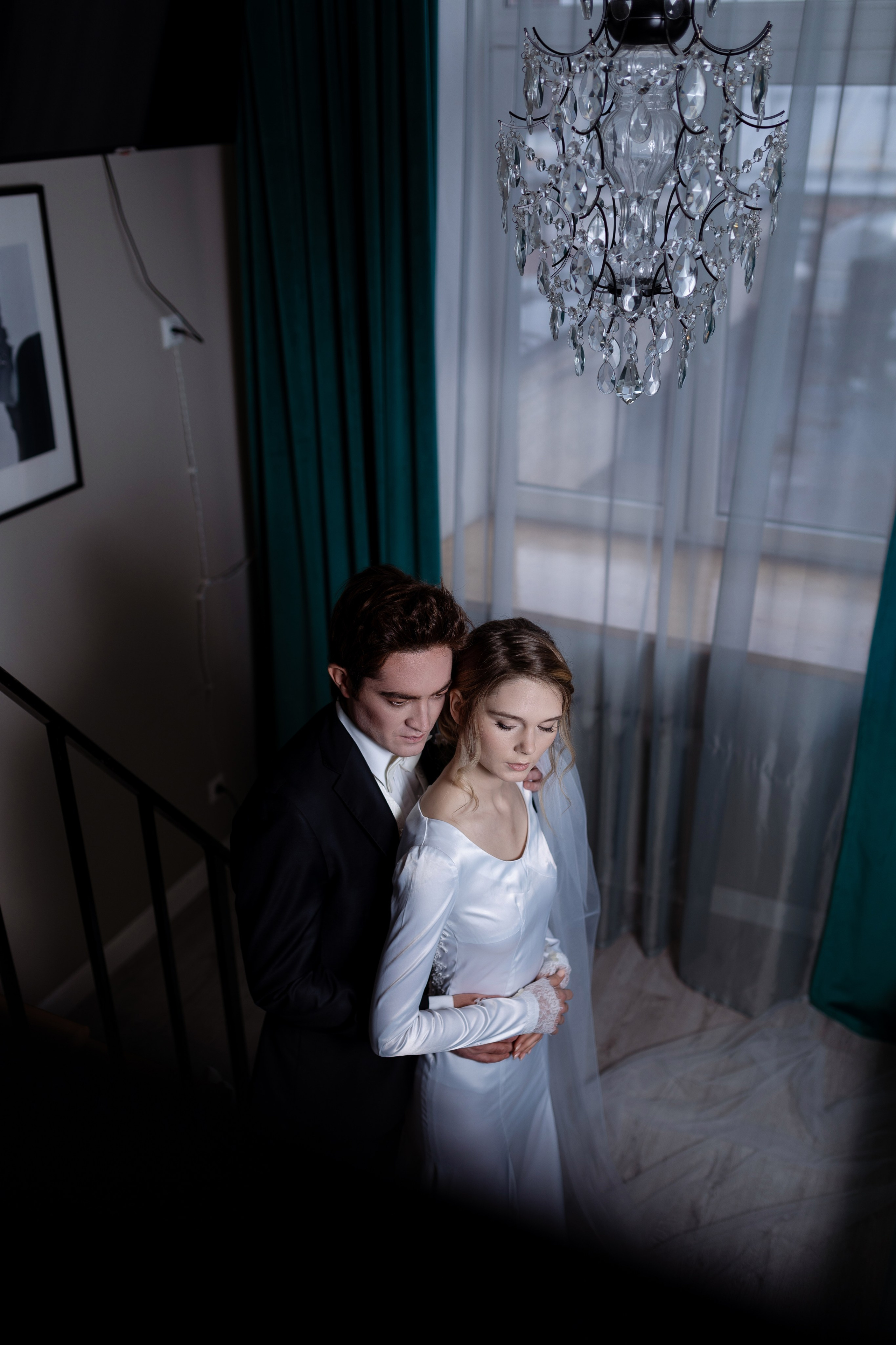 Жених и невеста стоят у окна на темном фоне.