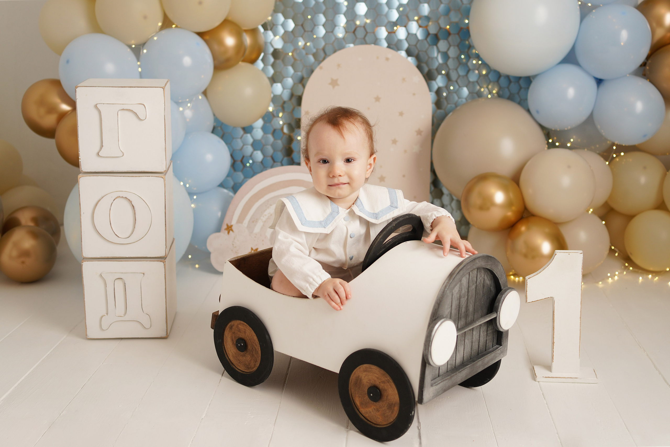 На фотосессии Первый годик малыш сидит  в машинке , рядом большие кубики год и цифра один.