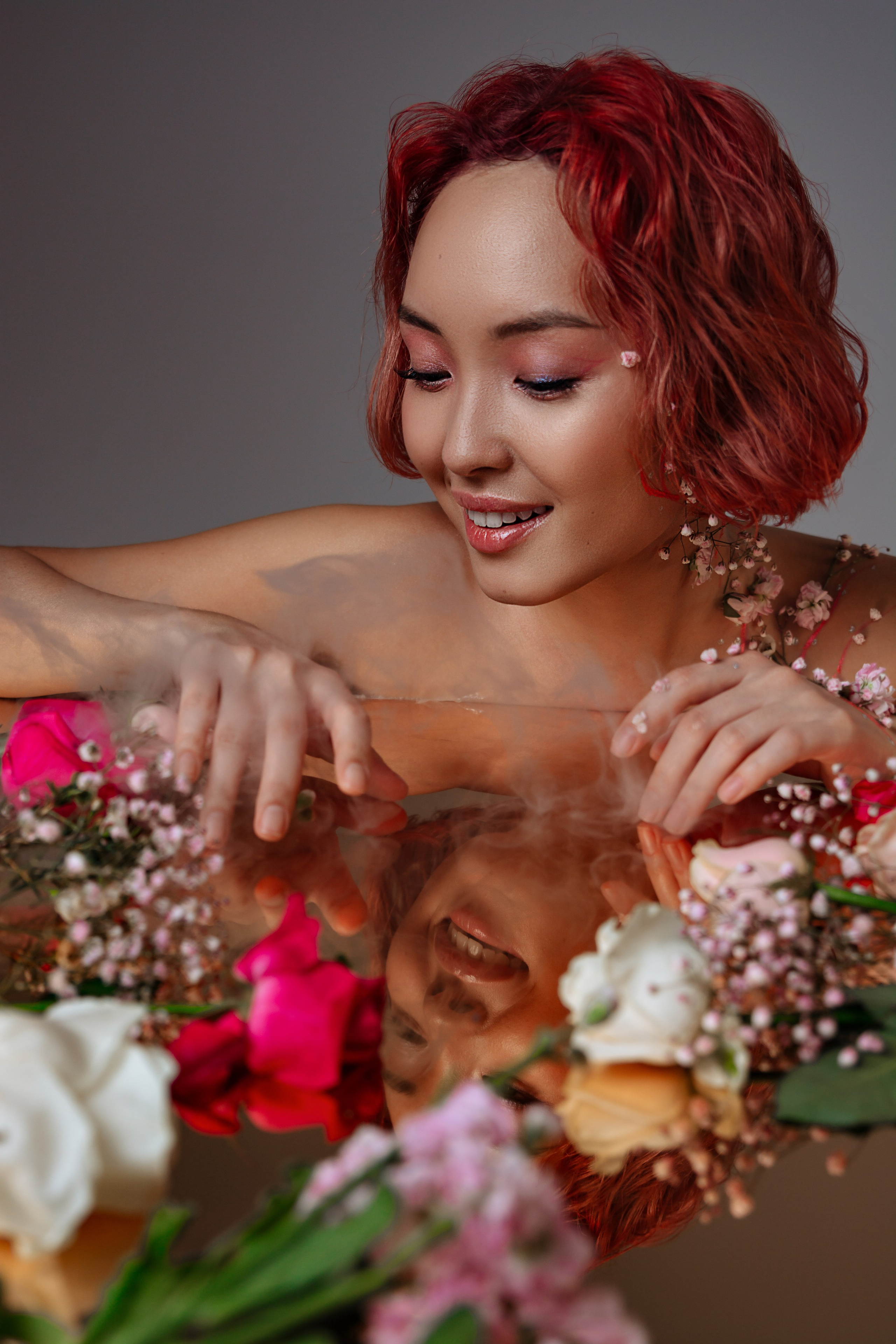 Окруженная живыми цветами на столе девушка в романтичном розовом наряде с цветочной вышивкой символизирует пробуждение природы после зимней спячки.