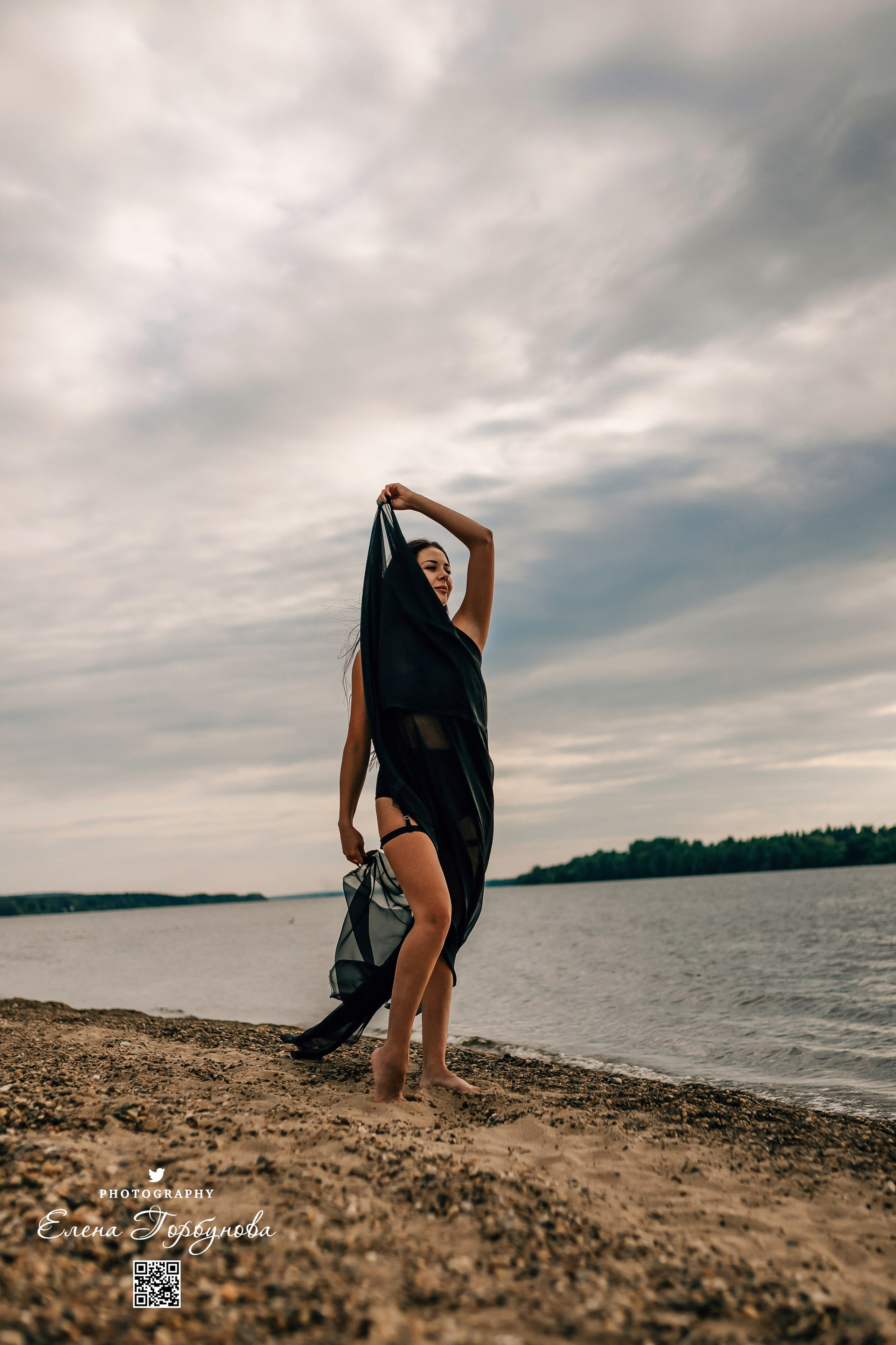 Фотосессия с черной тканью. Легкая черная вуаль летит на вертру. Фотосессия у реки черная серия с тканью. Девушка укуталась в черную ткань. Прогулка по набережной. Песок, речка, модель в черном. Качели над водой, Закат. Девушка лежит на песке. В зеленых деревьях