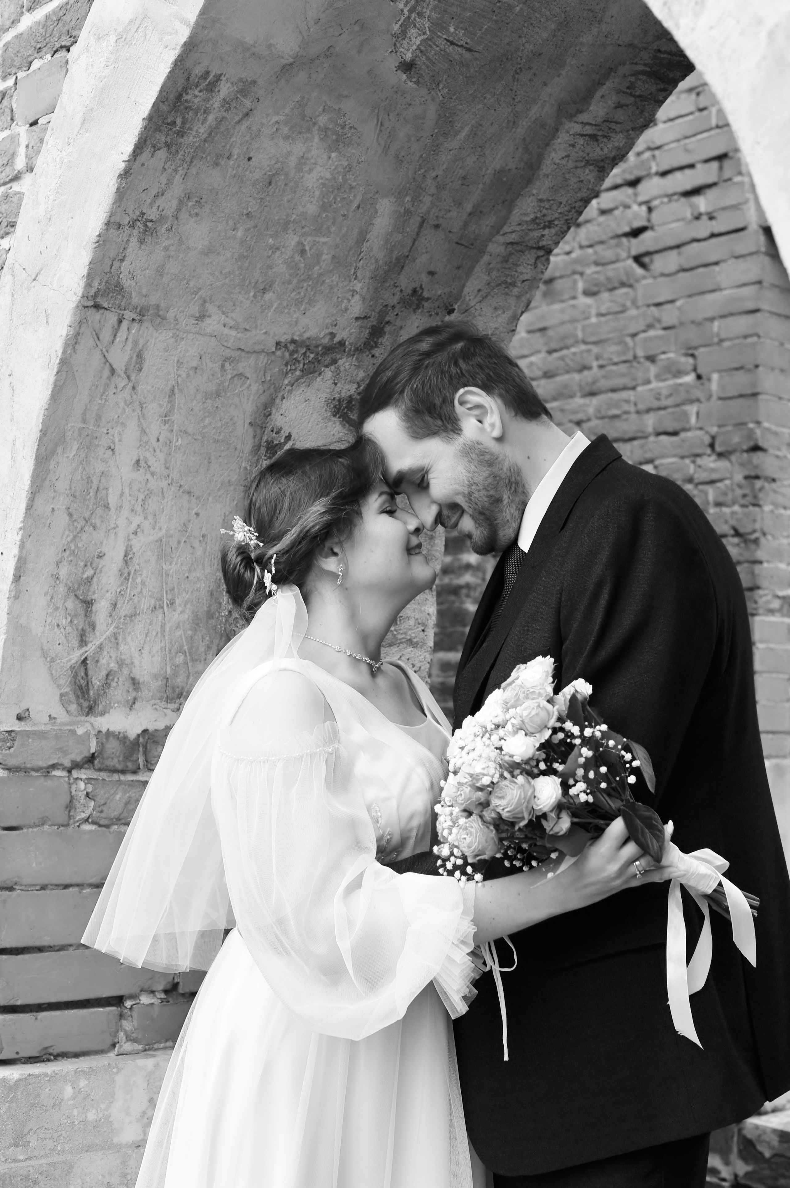 Свадьба в Царицыно пасмурным летним днем, новобрачные обнимаются в арке, черно-белая фотография 