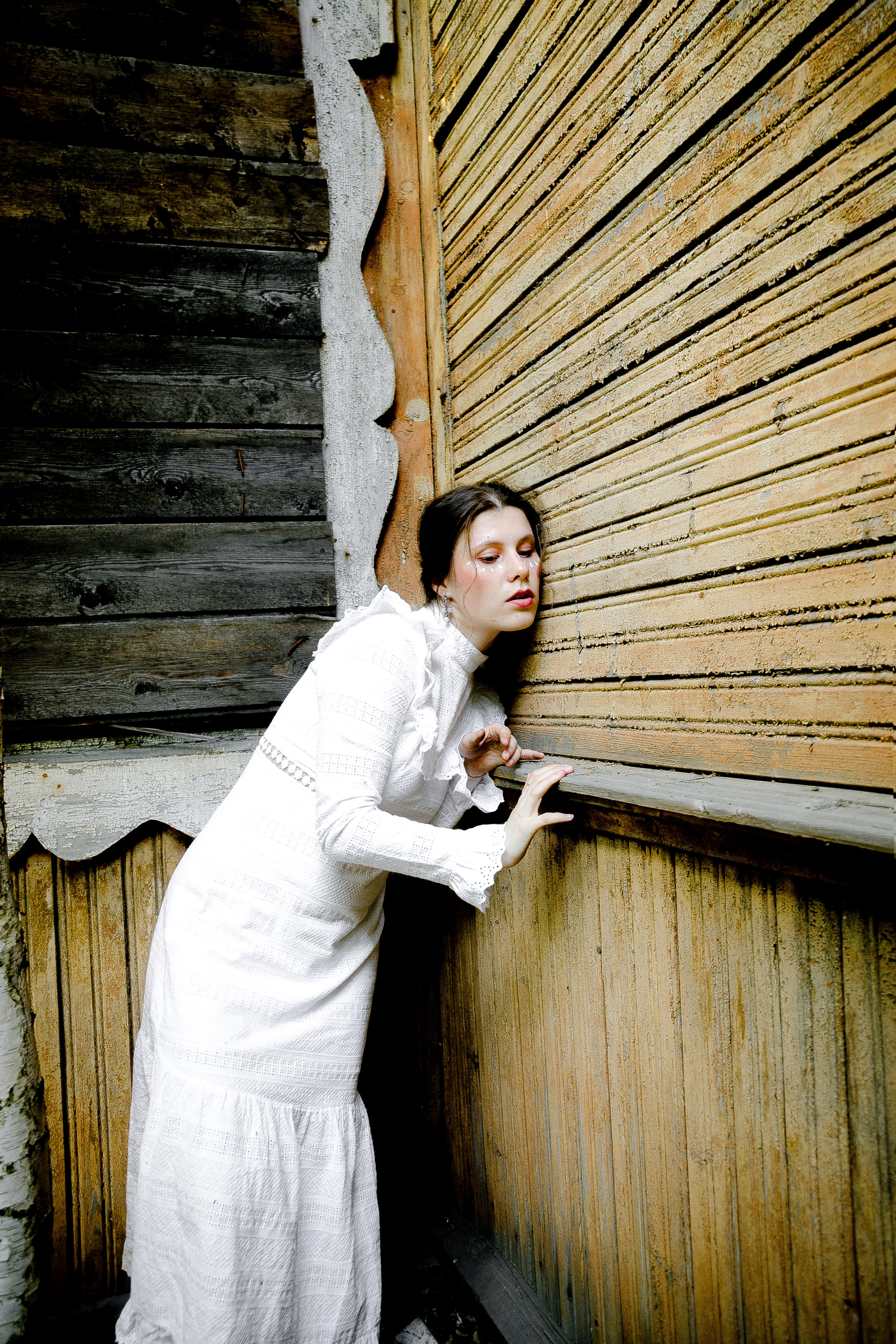 молодая девушка слушает стену желтого деревянного дома.