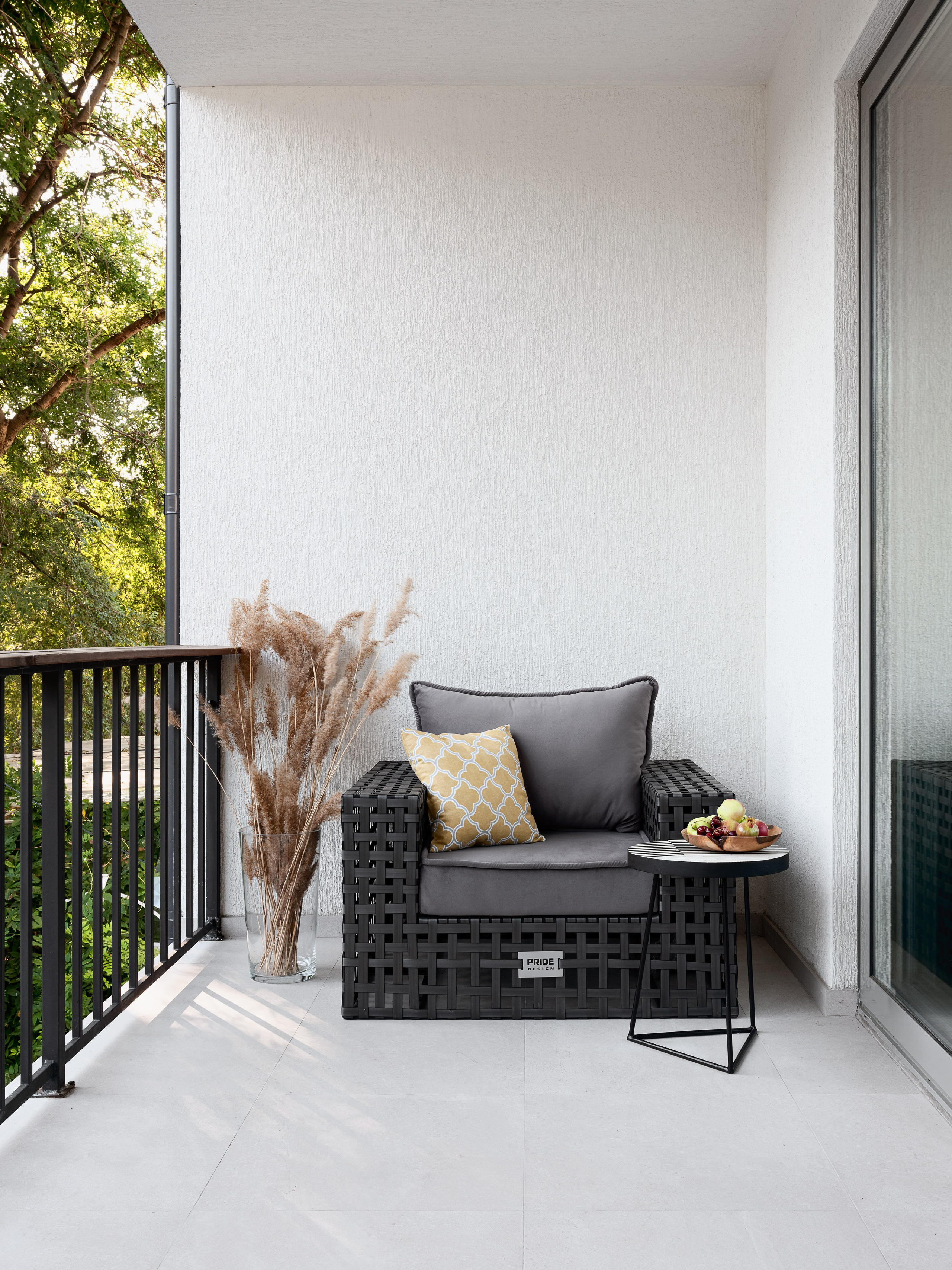 Уютный современный балкон с креслом из плетёного материала, серыми подушками и жёлтой декоративной подушкой, столиком с фруктами и вазой с сухоцветами, дизайн интерьера Алёна Попова и Анастасия Дмитриева, фотограф Сергей Денисенко.