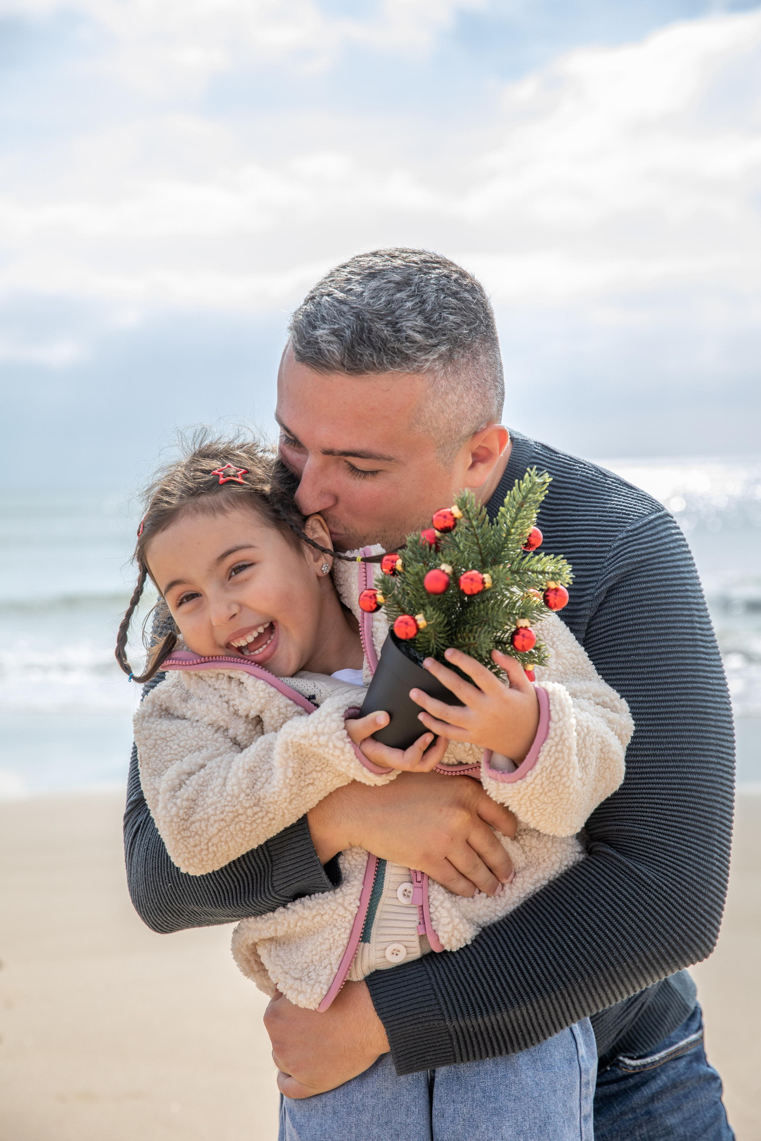 A sweet moment of connection, as dad and daughter share a hug with the ocean in the background.