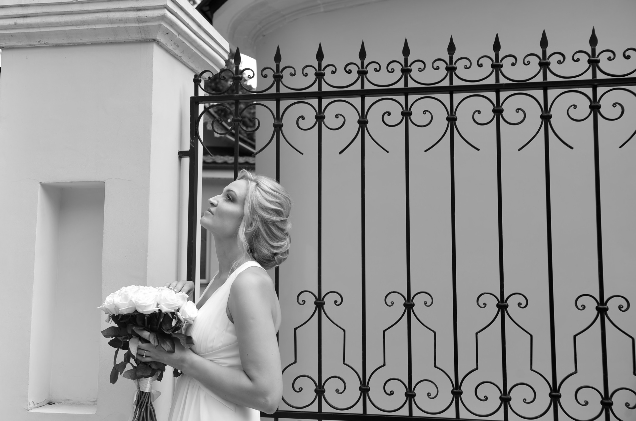 Свадьба на Воробьёвых Горах рядом с МГУ, невеста стоит у кованной ограды храма со свадебным букетом в руках, черно-белая фотография