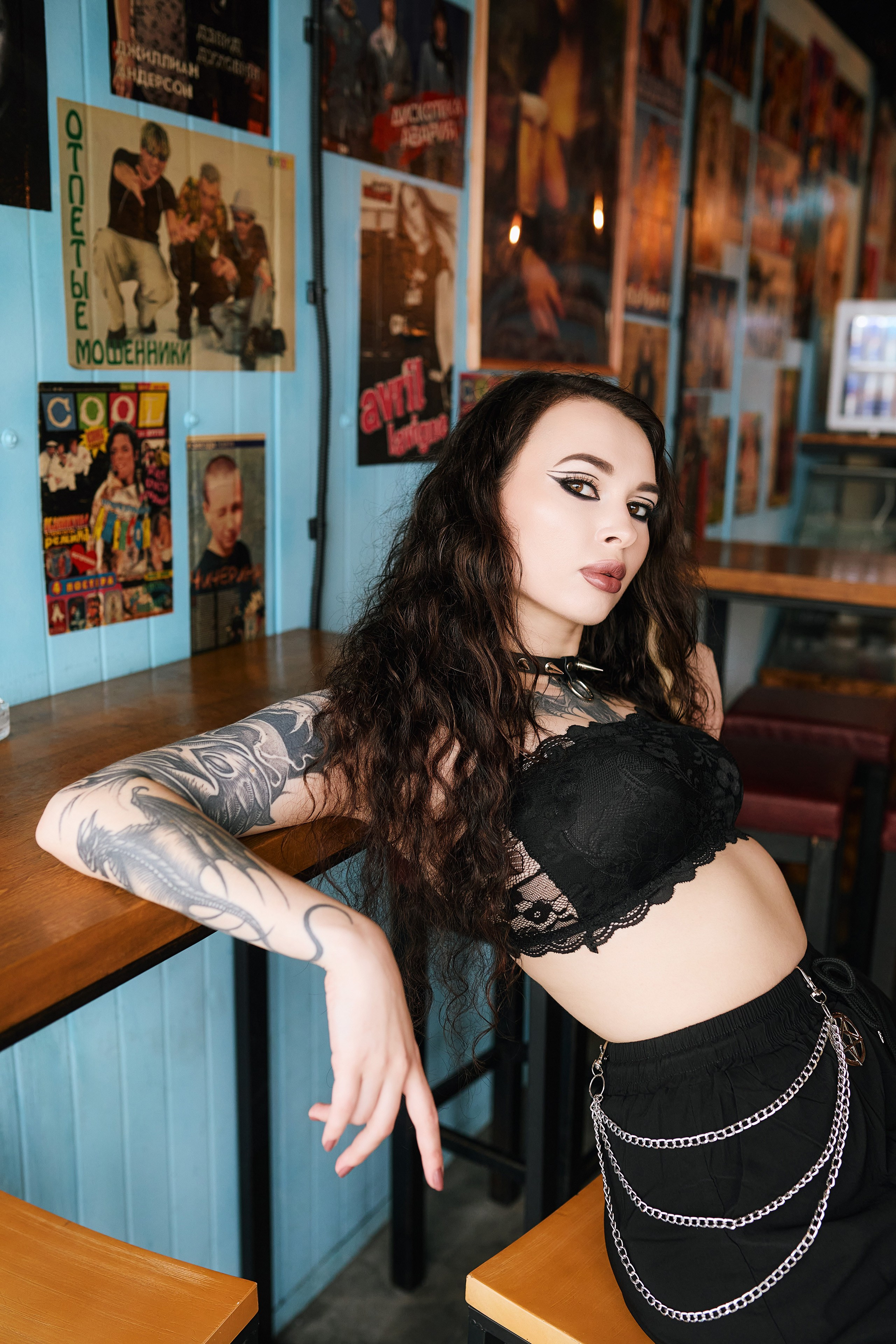 Портретная фотосессия во Владивостоке с красивой татуированной девушкой в чёрном топе и постерами рок-групп на фоне