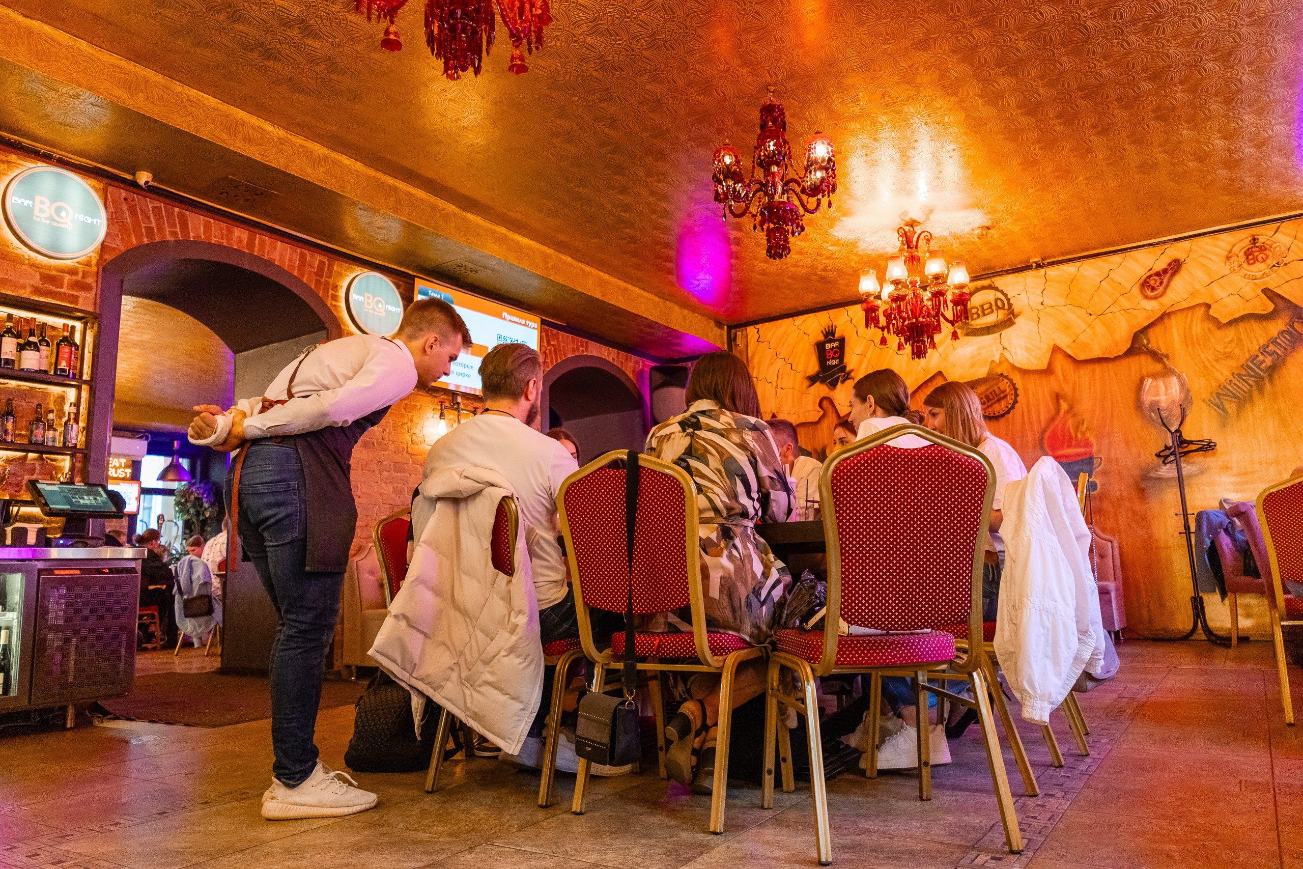 Официант бара Bar BQ Night обслуживает столик с игроками игры квиз