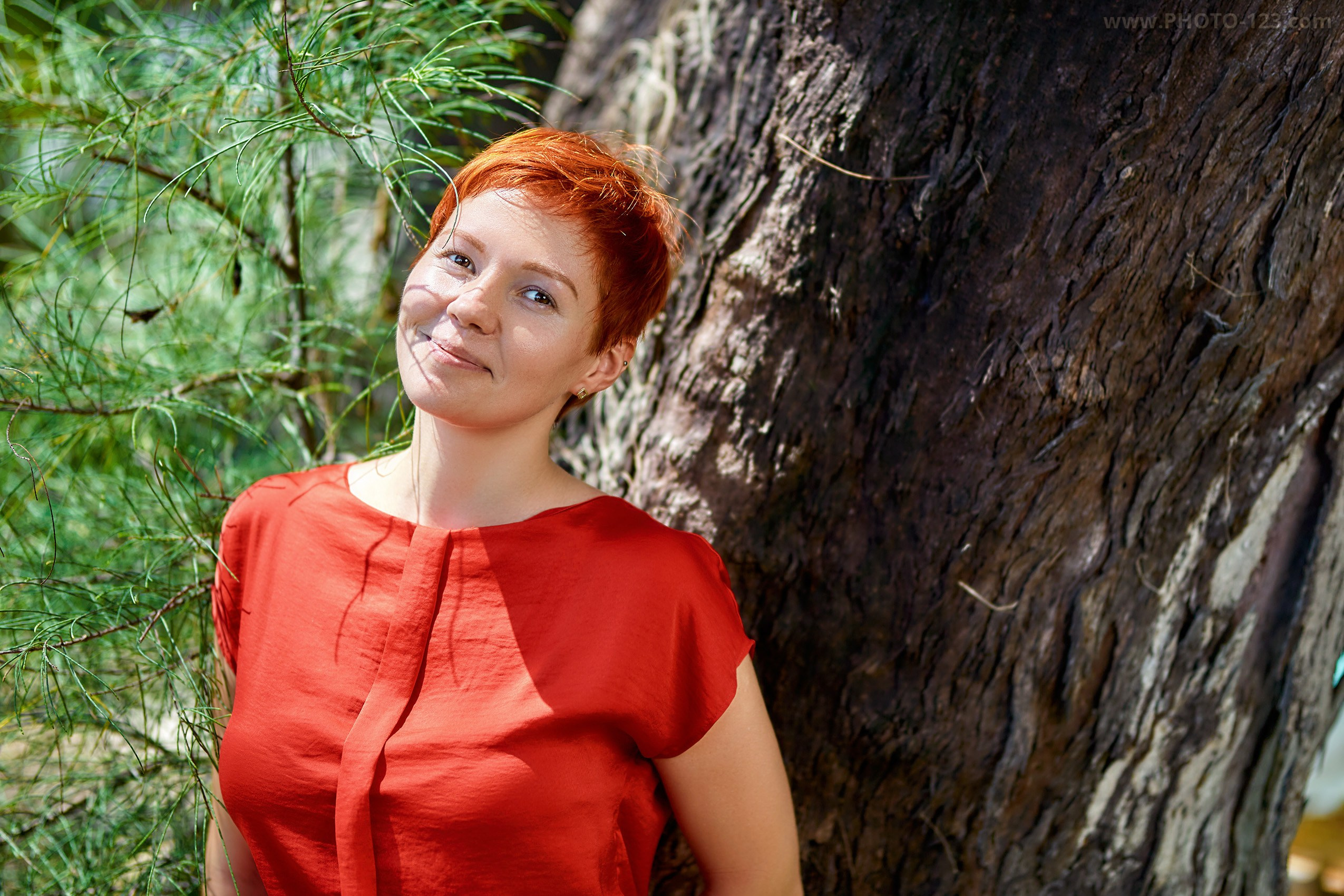Portrait of a woman with short red hair standing by a tree in tropical nature, natural light portrait photography in Phu Quoc, Vietnam, relaxed and authentic mood