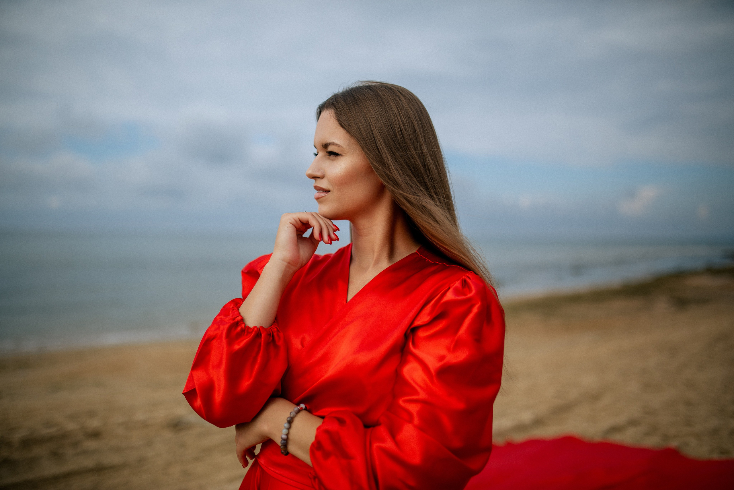 Девушка в красном платье стоит на пляже Джемете в пасмурную погоду.