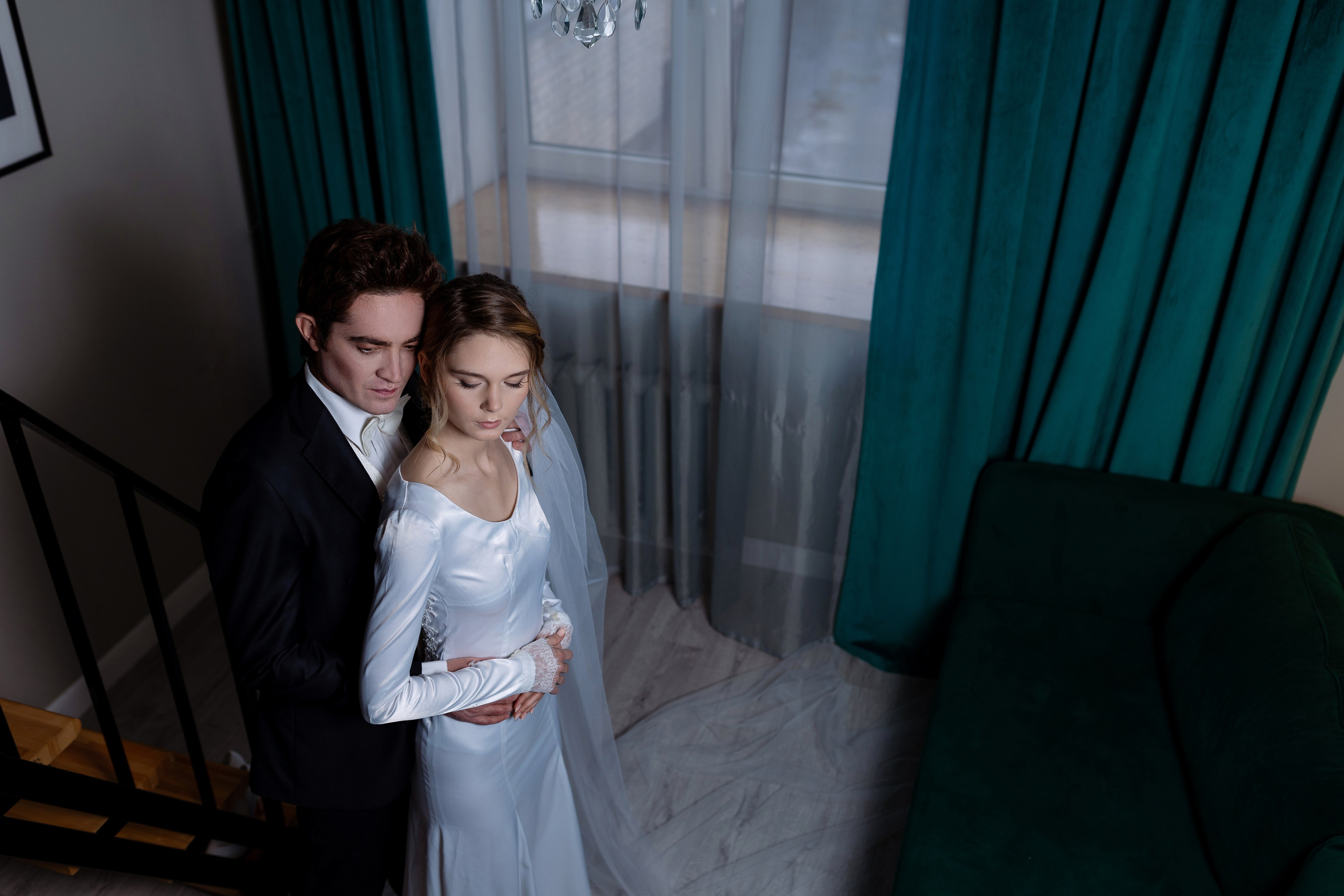 Жених прижал к себе невесту на темном фоне у окна.