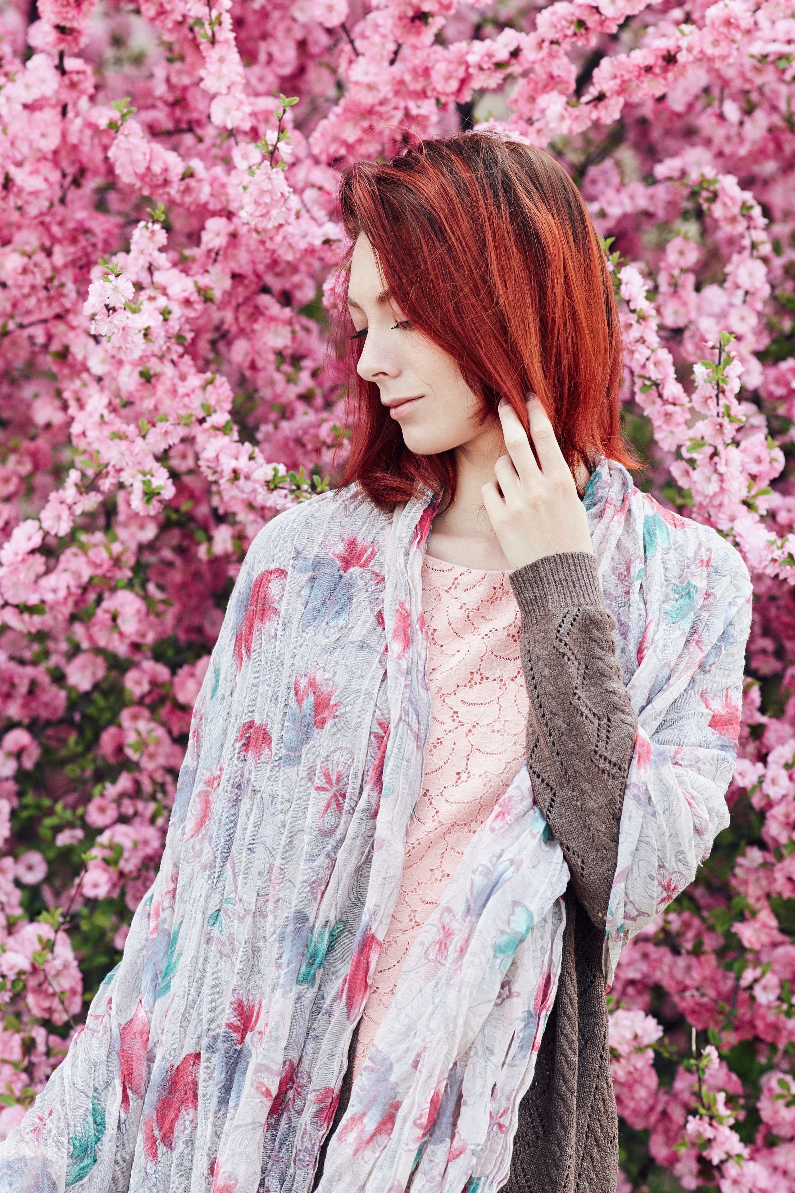 Задумчивая рыжеволосая модель позирует в платье на фоне цветущего миндаля