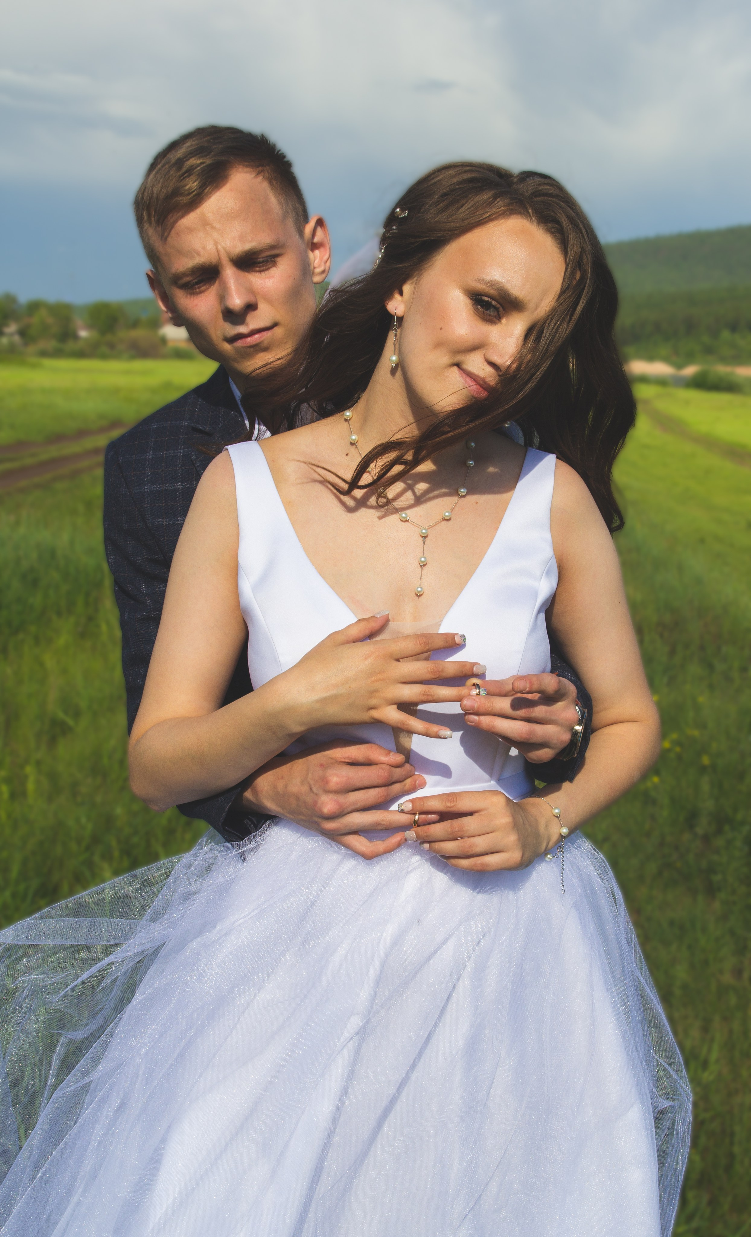 Жених обнимает невесту в поле — романтический и тёплый кадр с природным фоном.