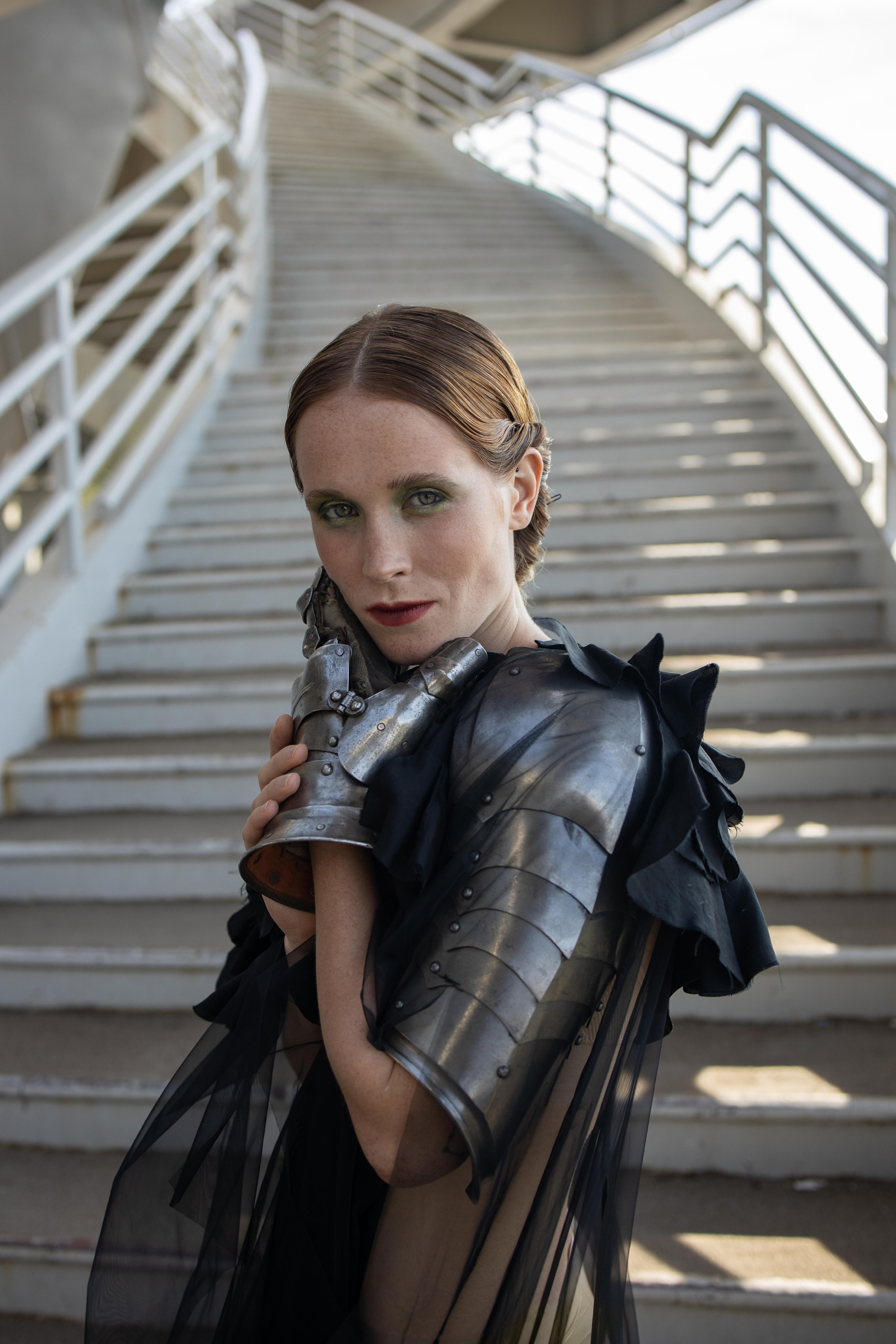Девушка в доспехах на руках стоит на фоне лестницы