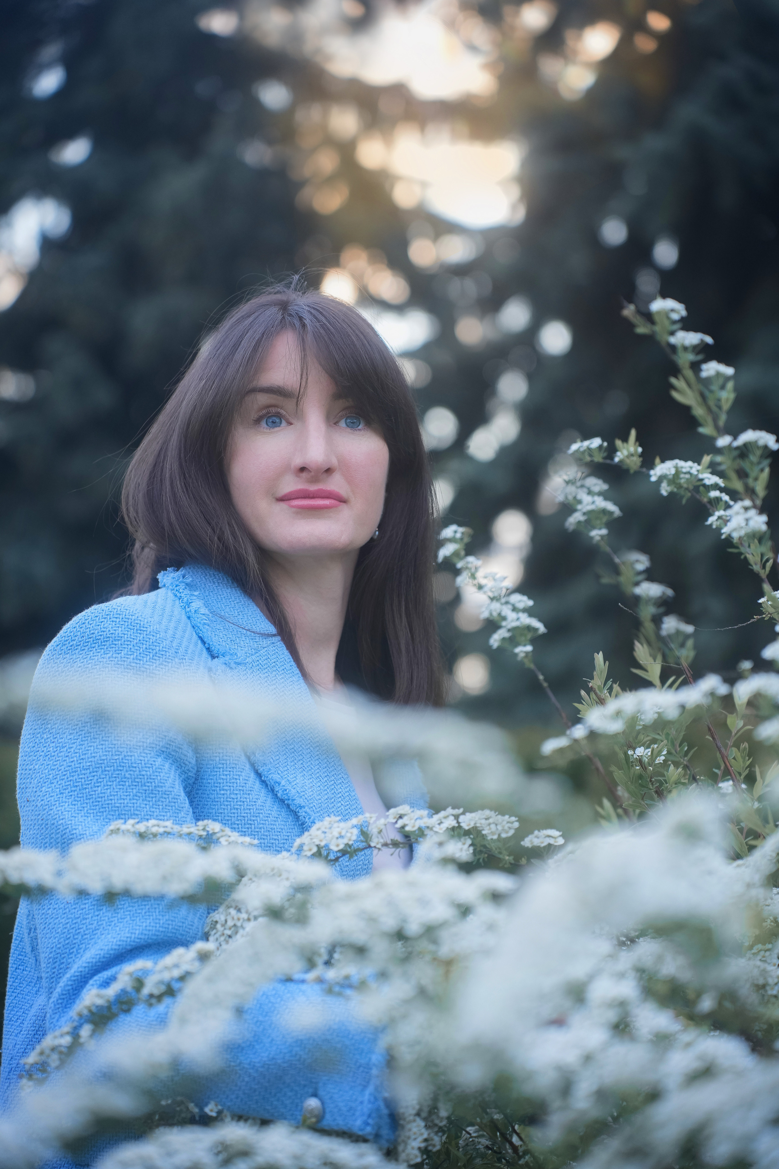 Красивый портрет молодой женщины с темными волосами на фоне белых цветущих кустов на закате