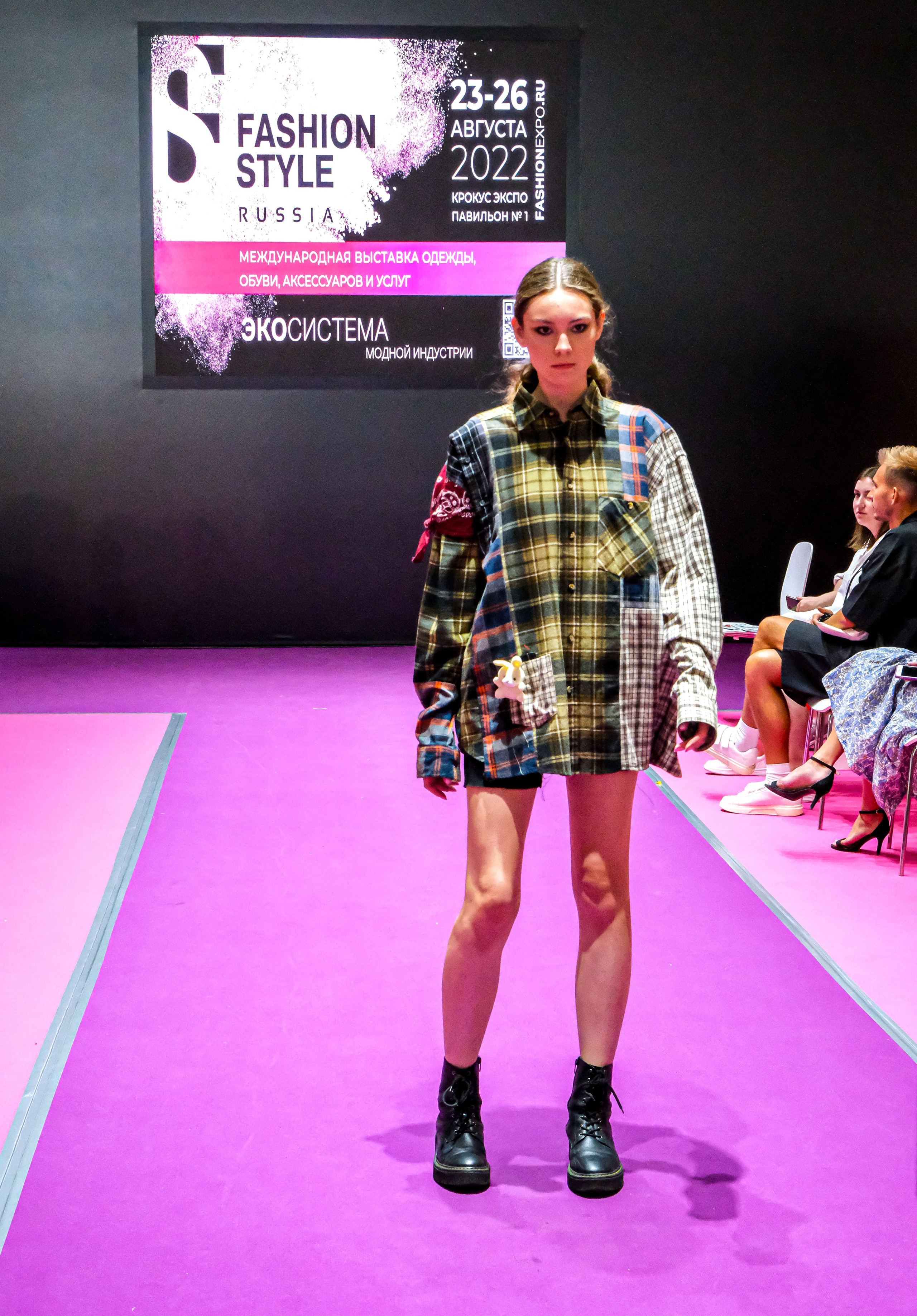  "Модели в ярких нарядах проходят по подиуму во время показа мод, освещенные яркими софитами и окруженные восторженными зрителями."