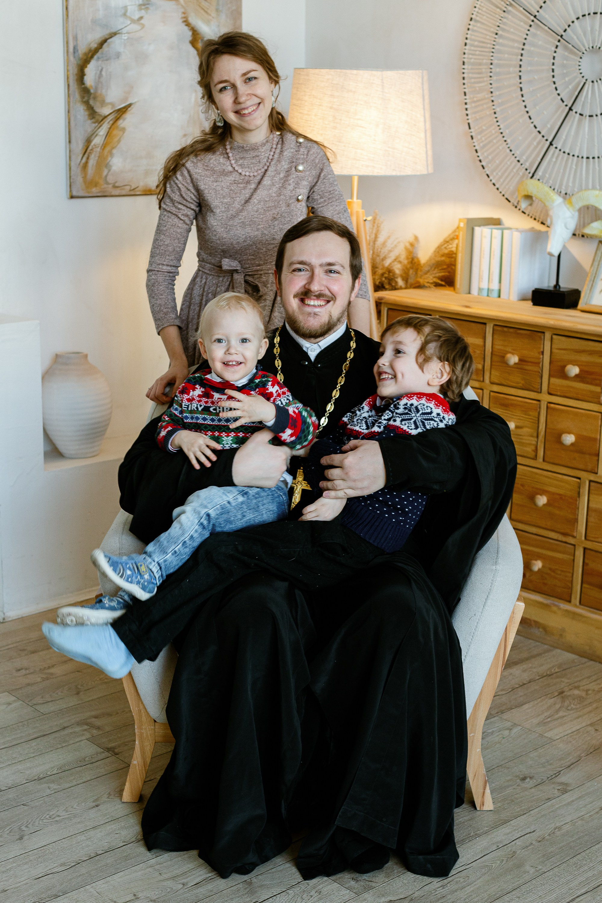 Семья священника. Отец сидит на кресле с детьми, жена стоит возле него.