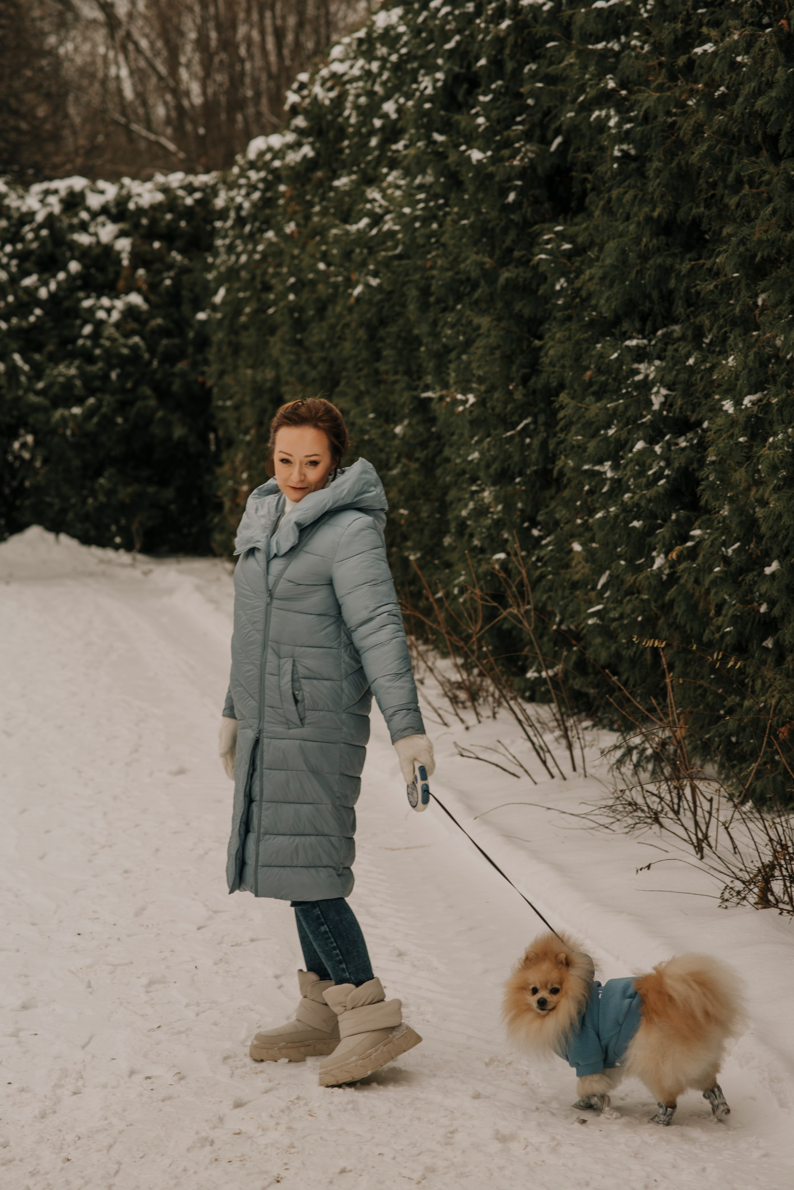  Девушка в голубой куртке гуляет с собакой шпицем на поводке по зинему лему