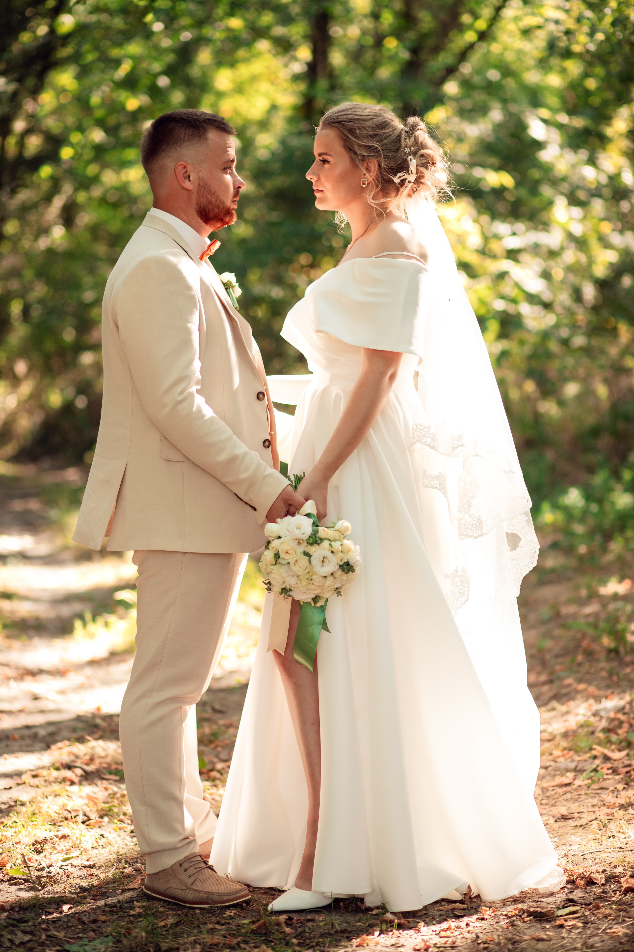 Молодожены стоят лицом друг к другу держась за руки