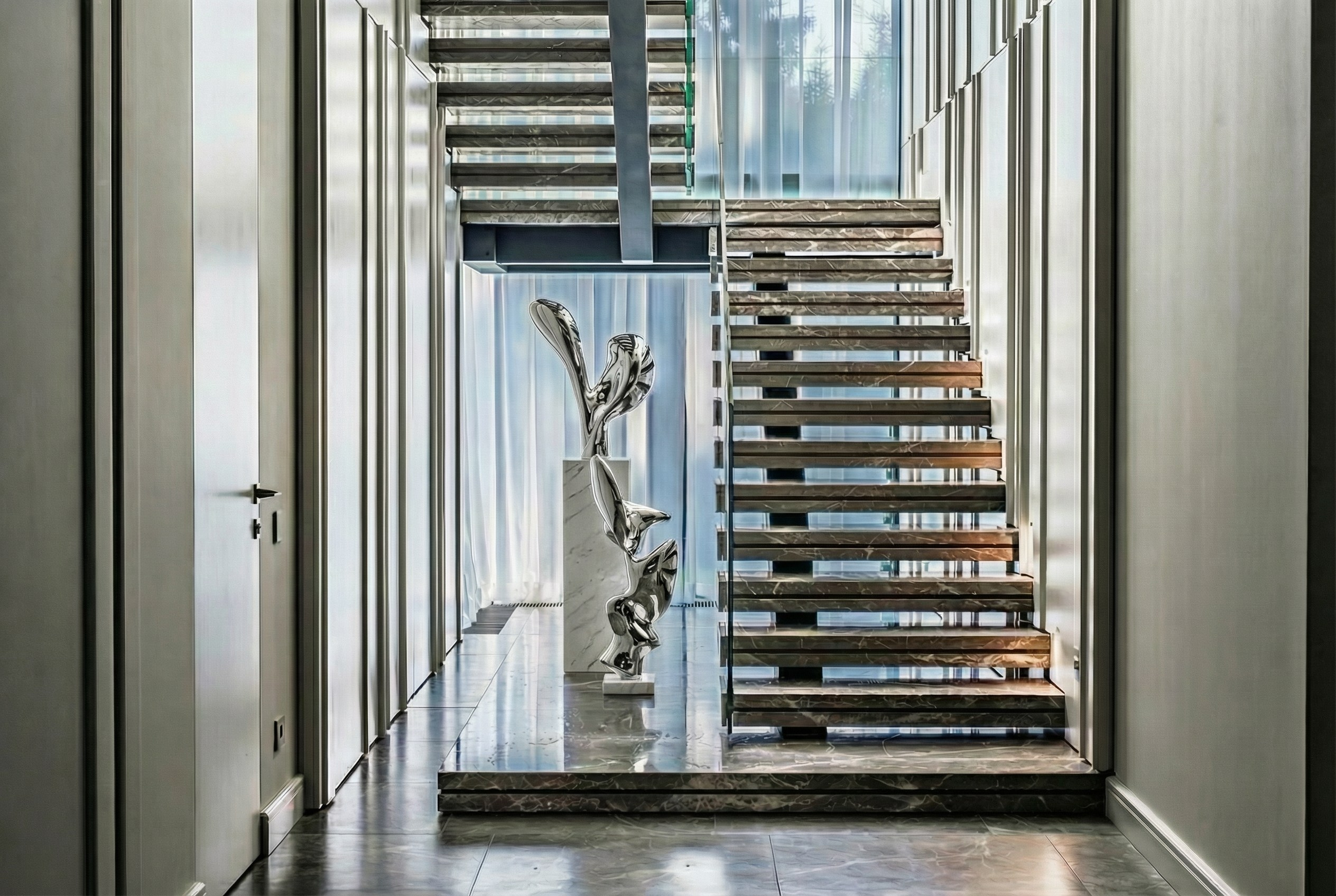 Парадная лестница с консольными мраморными ступенями и арт-объектом в холле, панорамное остекление и дизайнерские стеновые панели, проект Валерии Котович в Подмосковье.