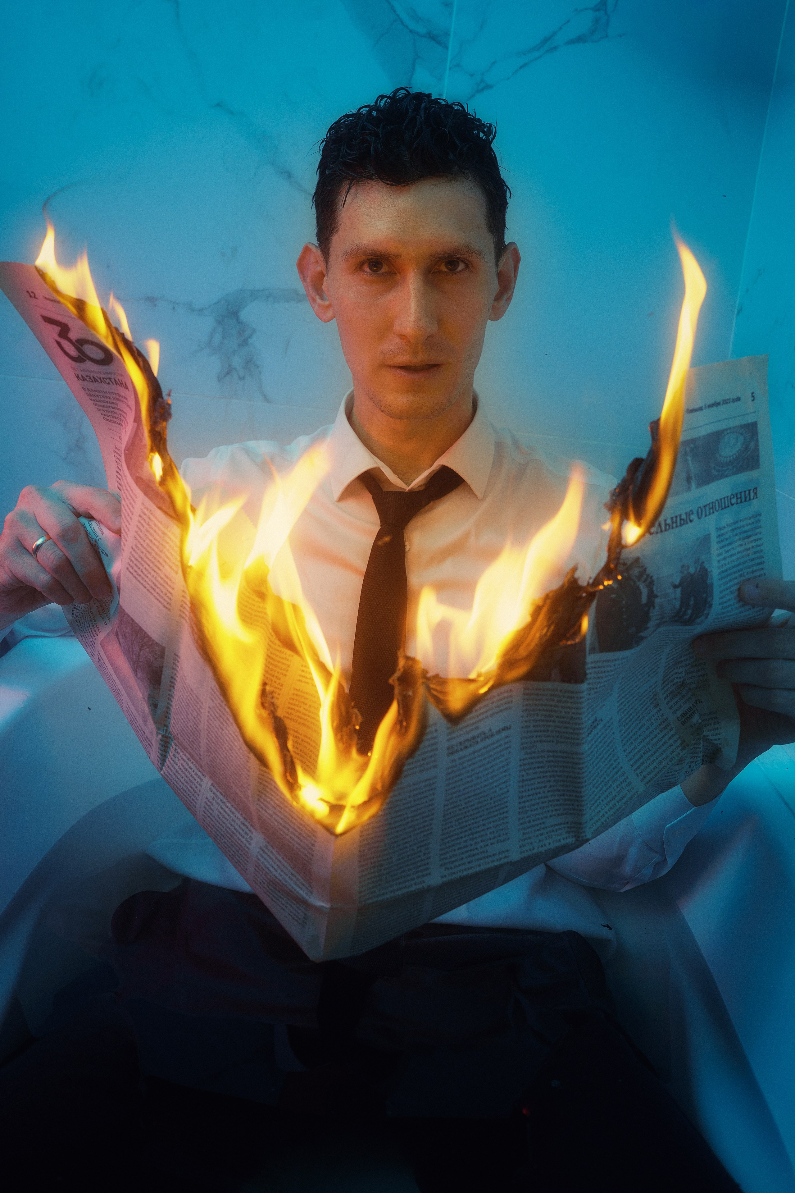 Мужчина в рубашке и галстуке читает горящую газету, символ выхода из зоны комфорта