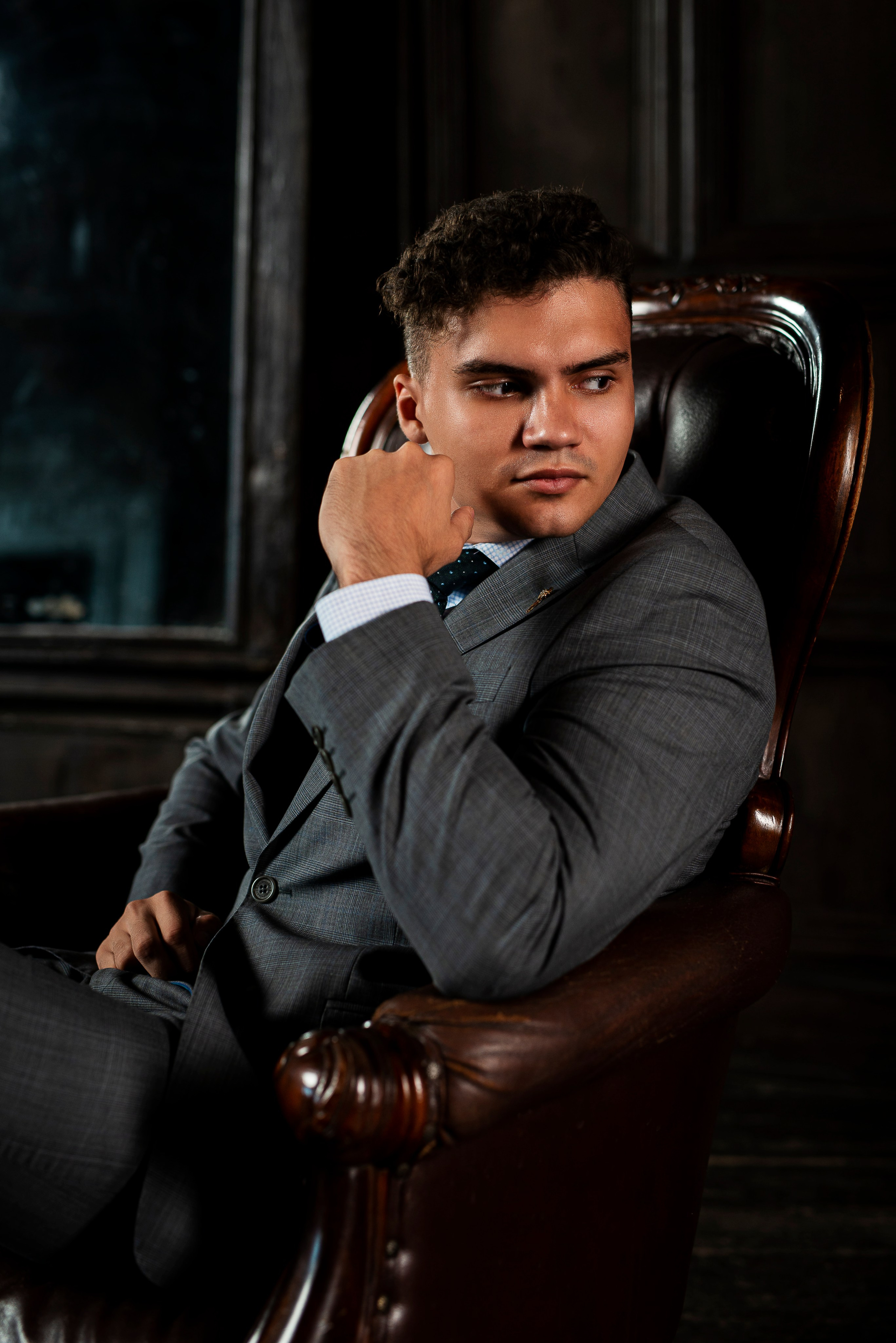 Молодой человек в деловом костюме позирует во время фотосессии сидя в кресле