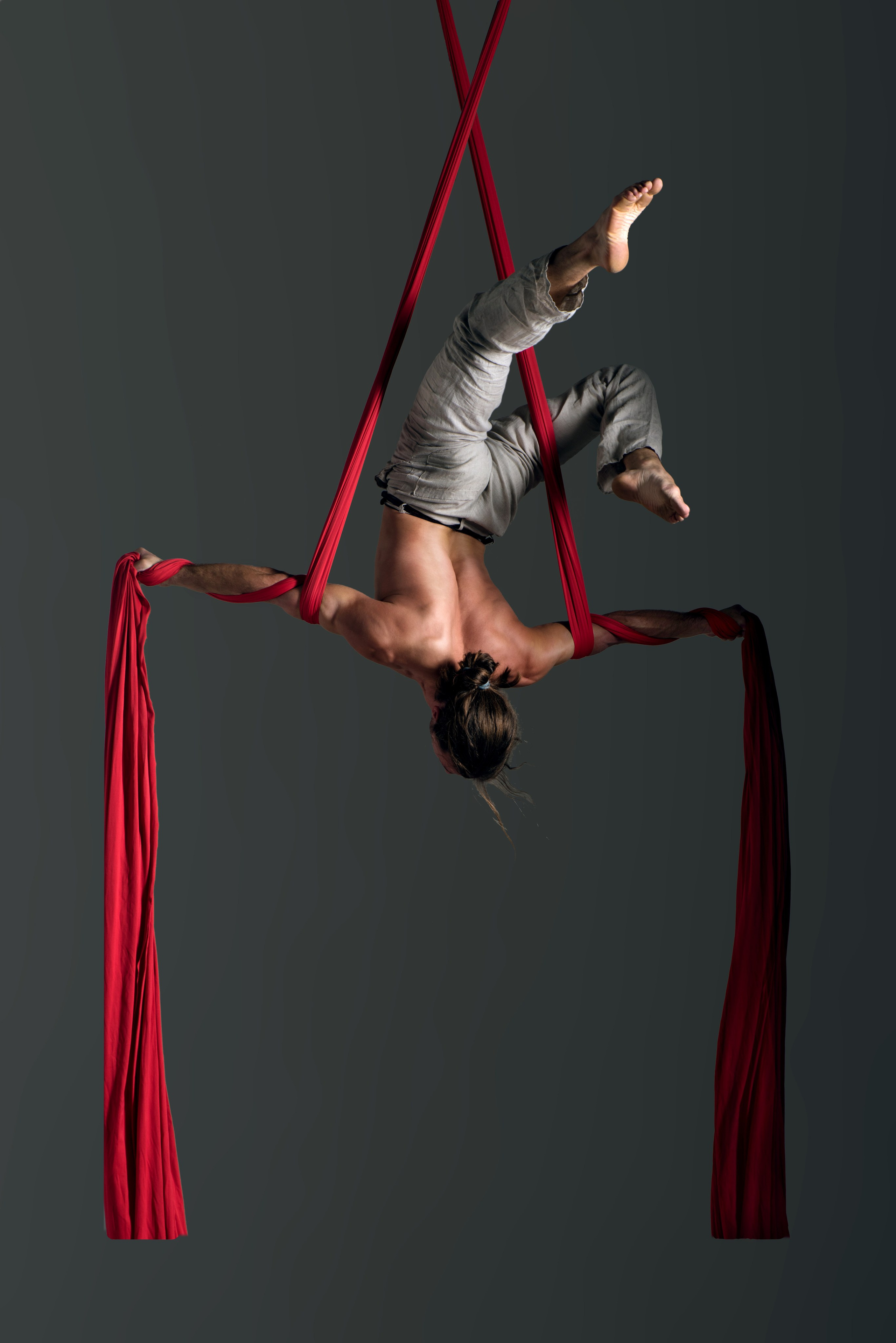 Профессиональная фотосъёмка циркового артиста, выполняющего трюк на воздушных красных полотнах. Движение, пластика, спортивная физика — художественный рекламный кадр.