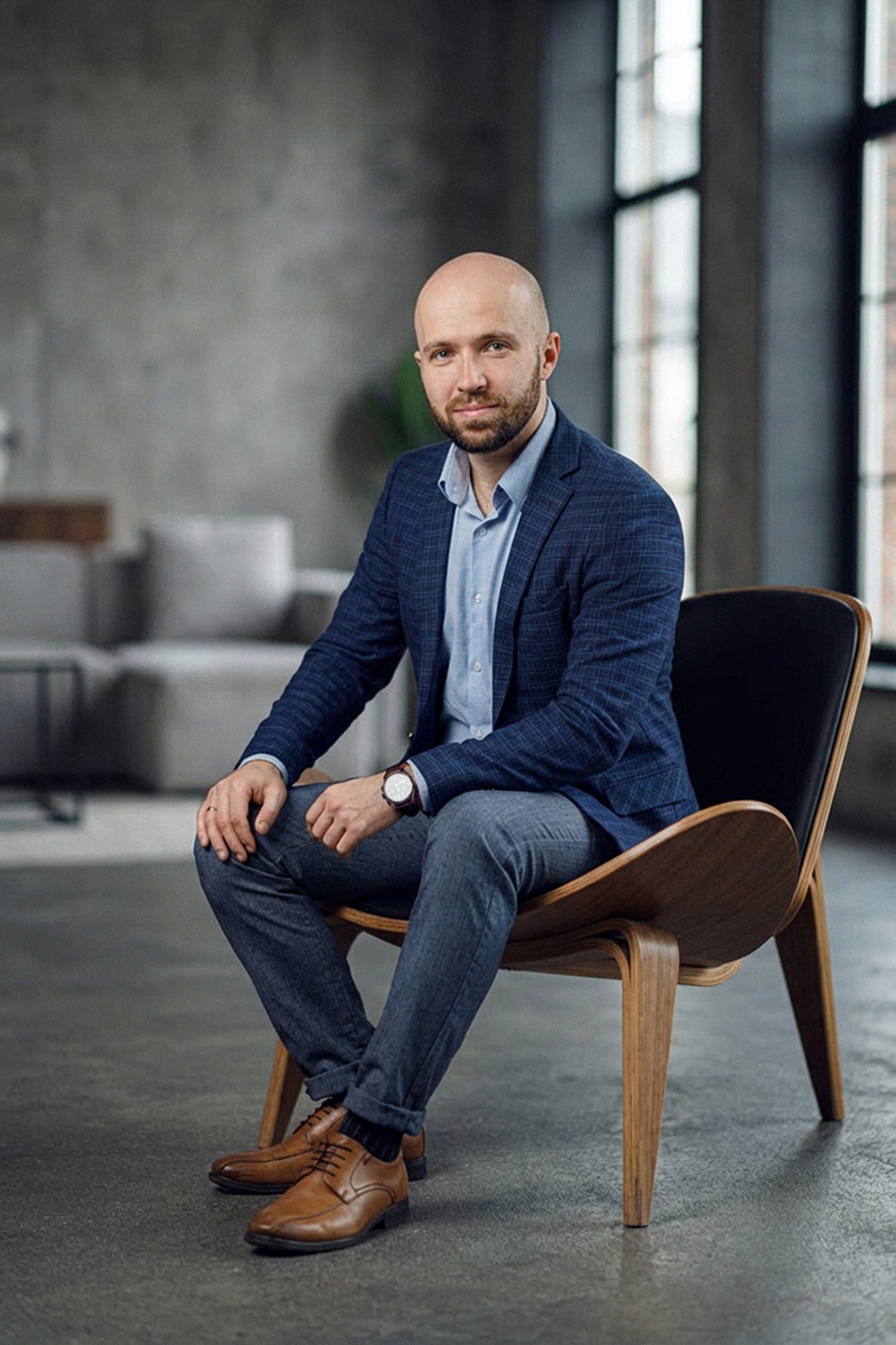 Мужчина в стиле business casual сидит на фоне кирпичной стены в лофте.