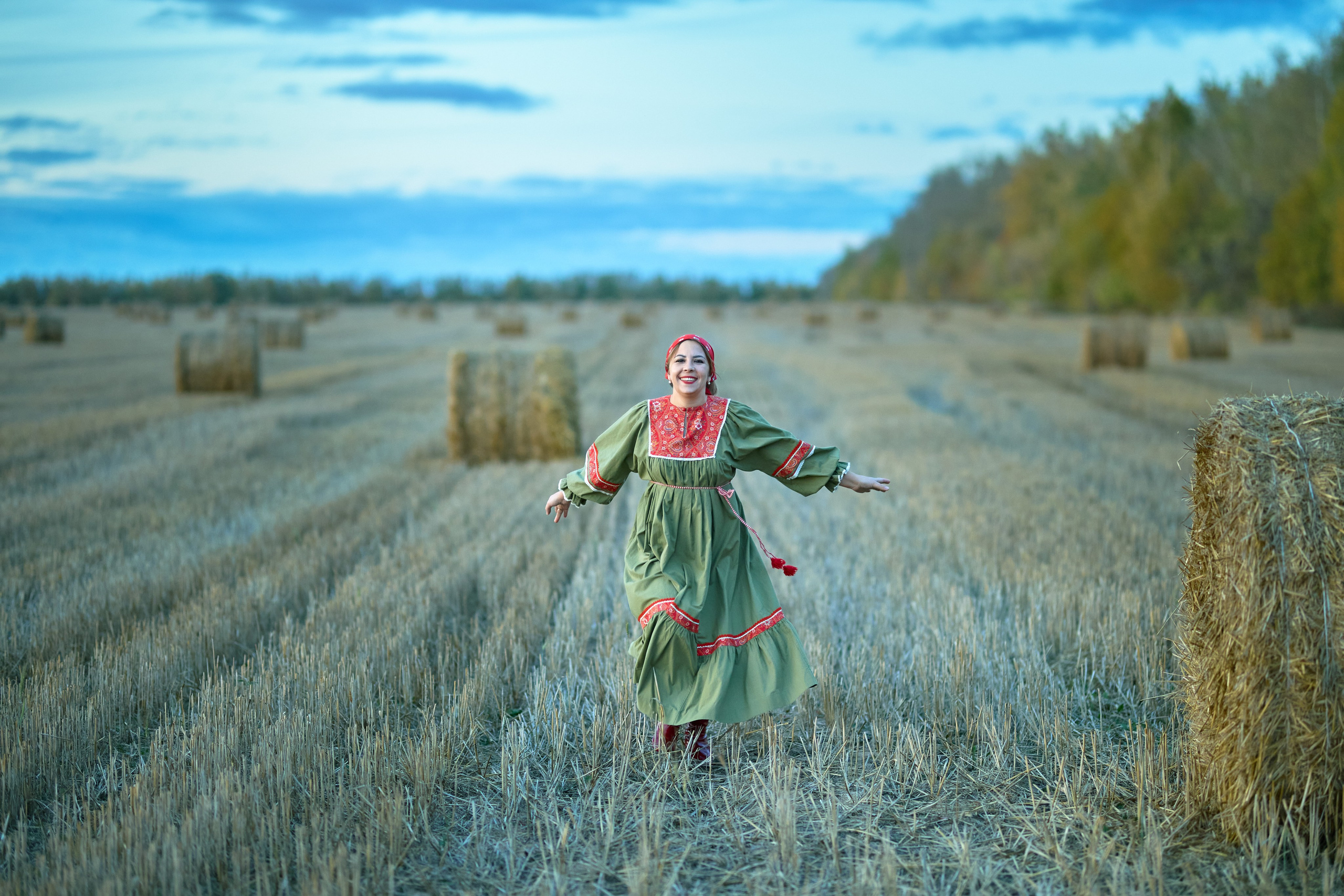 Женщина в национальном костюме бежит по убранному полю