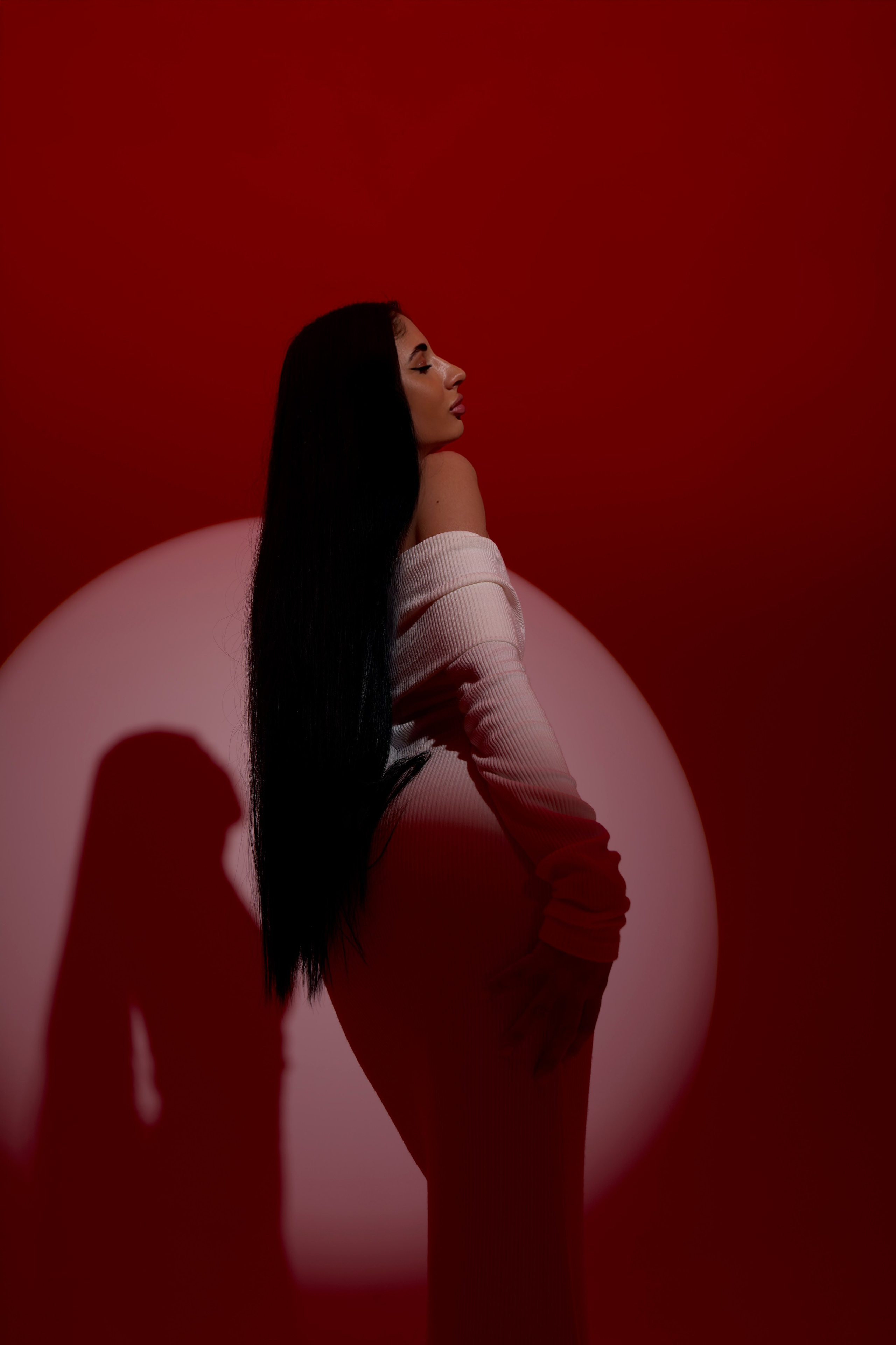 Портретная fashion-съёмка в Москве: женская фигура в профиль, световой круг и насыщенный красный фон