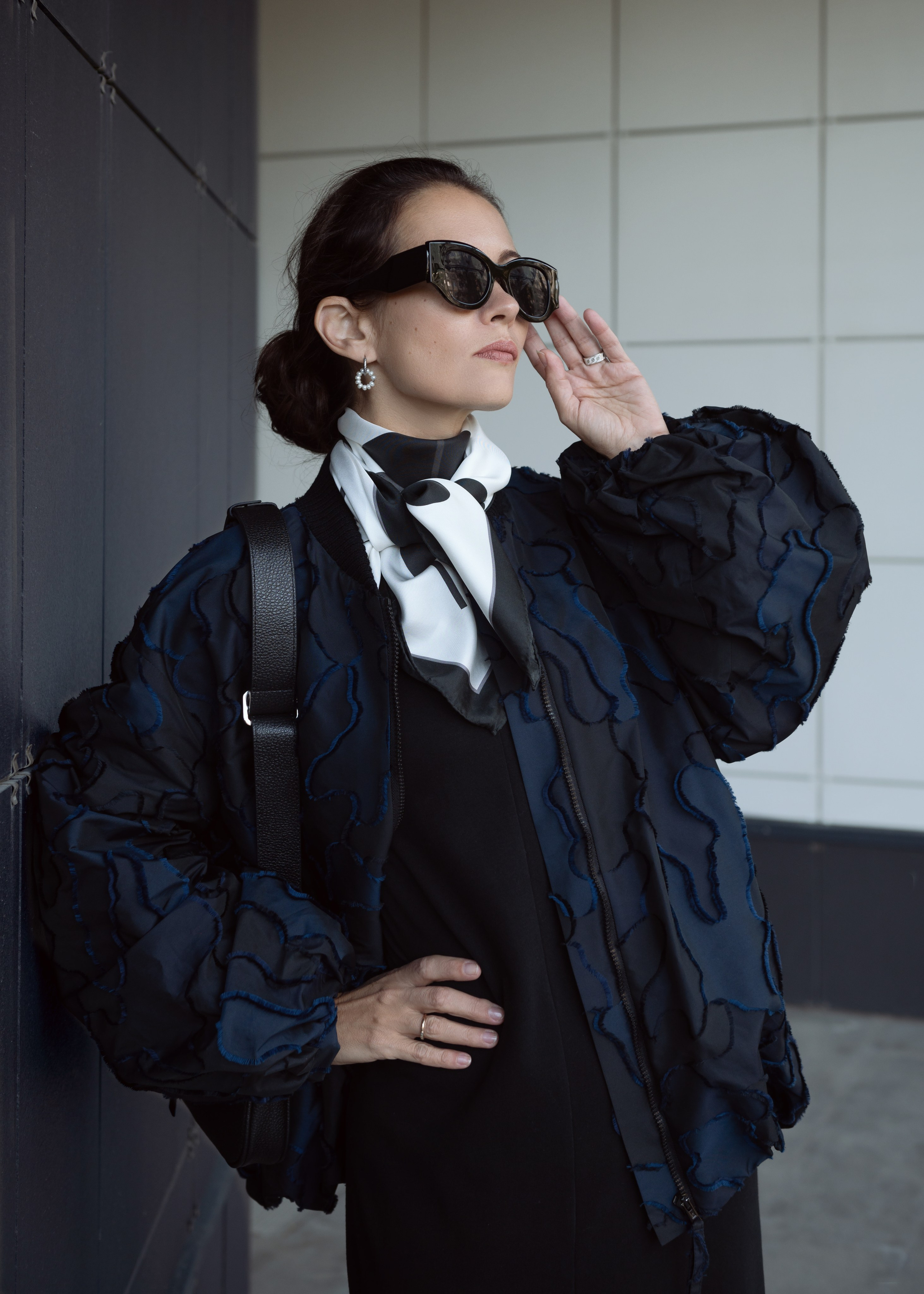 Девушка смотрит вдаль, она одета в темно-синий бомбер, черное платье и шелковый платок. Съемка для магазина женской одежды и аксессуаров