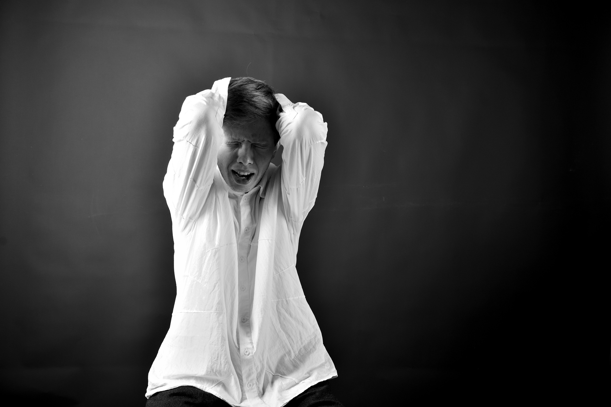 Мужчина закрывает ладоням лицо на фотографии в черно-белом стиле.