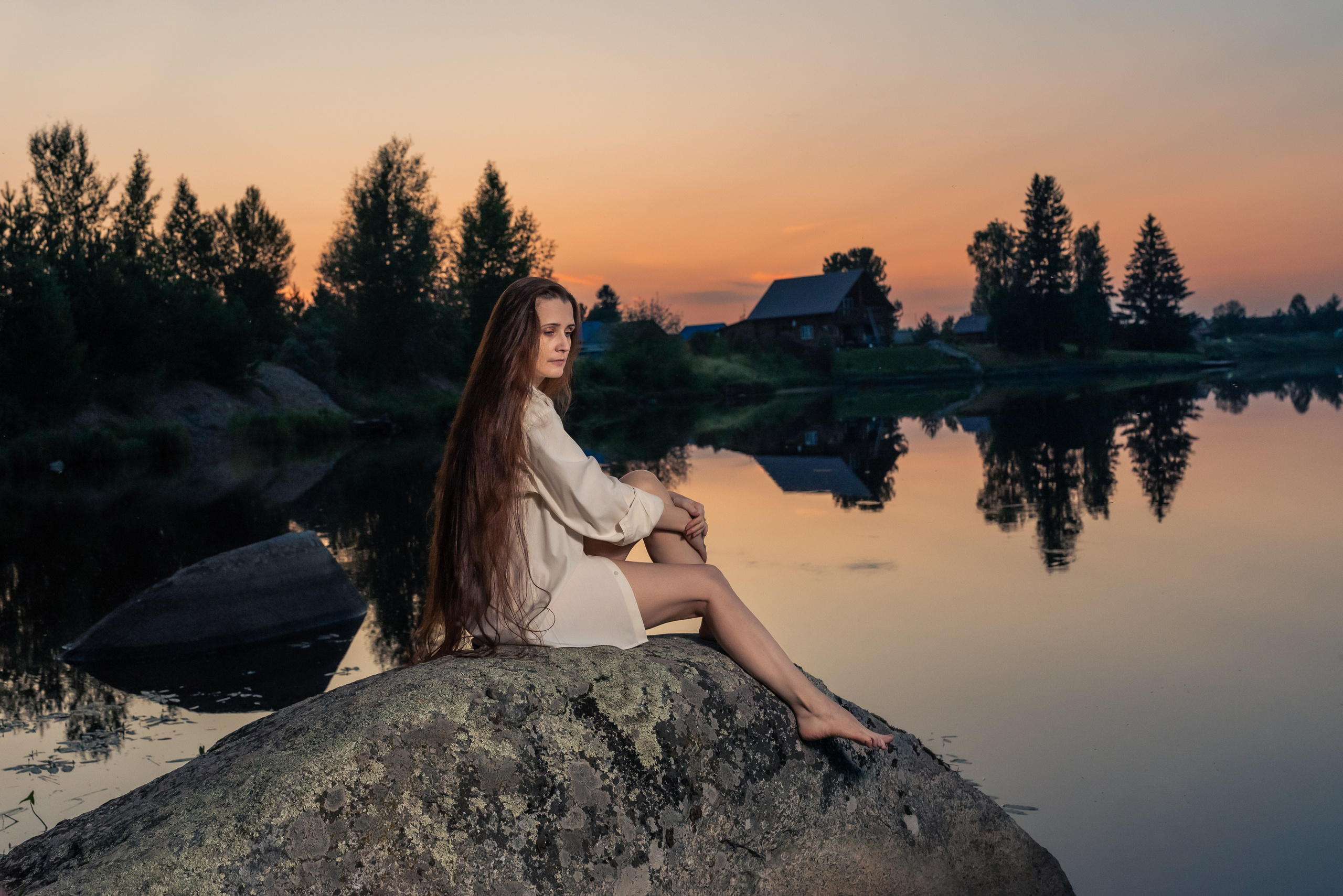 Летняя фотосессия. Девушка в длинной рубахе сидит на берегу реки на закате