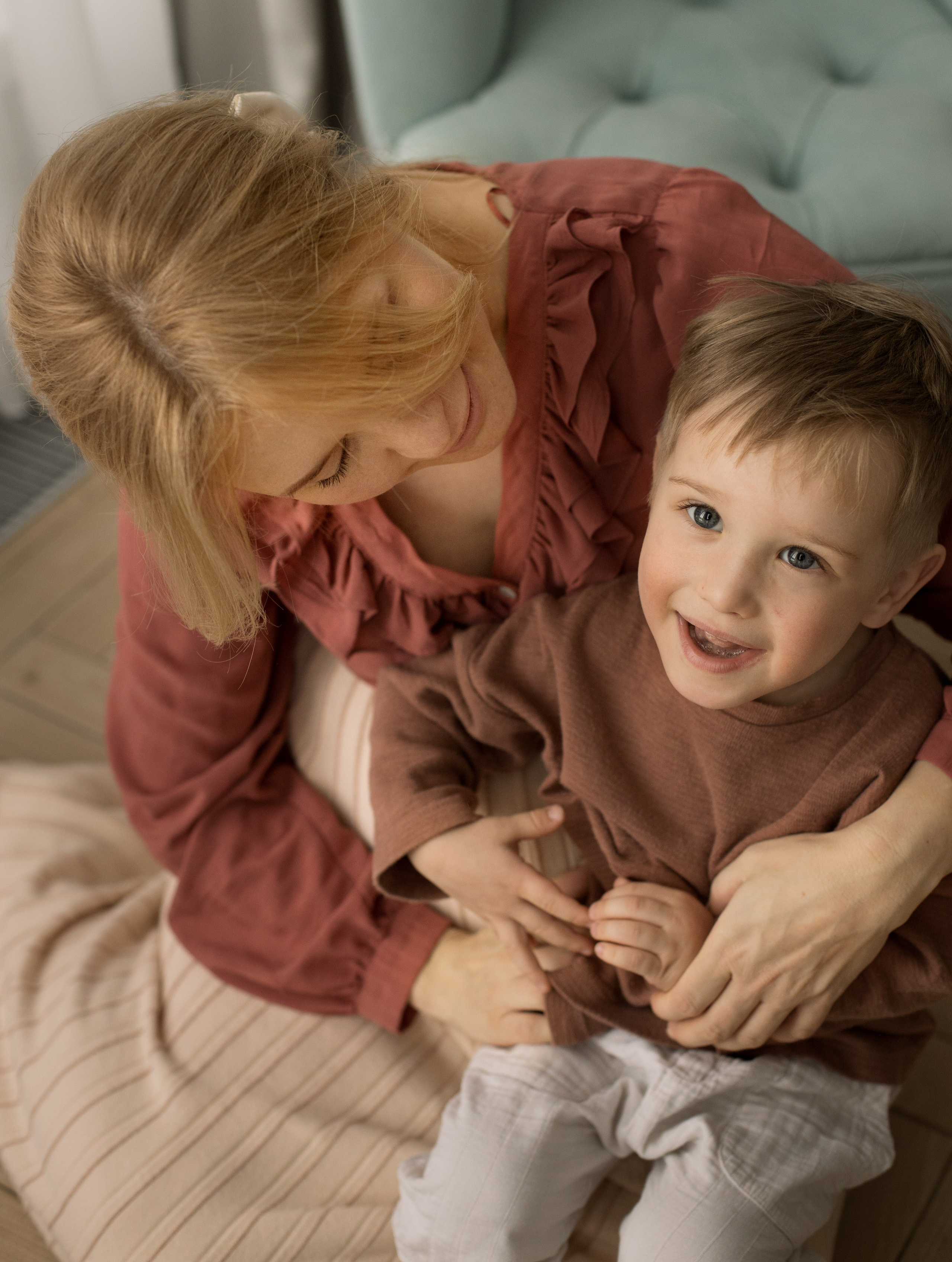 Беременная мама обнимает улыбающегося сына, сидя на полу.