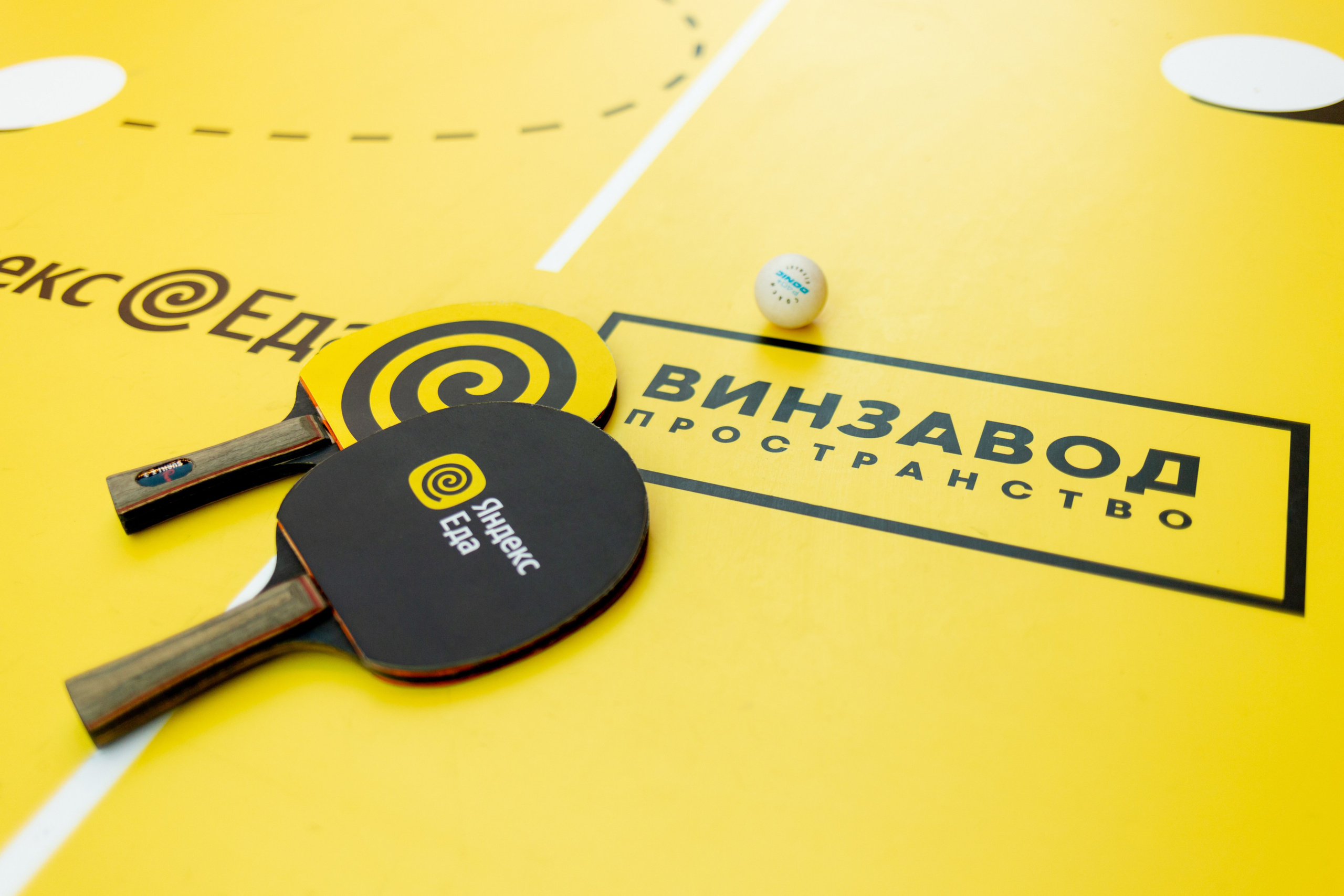 Желтый стол для настольного тенниса. Все ракетки для настольного тенниса лежат на столе. Настольный теннис Яндекс.Еды и Винзавода в Воронеже.