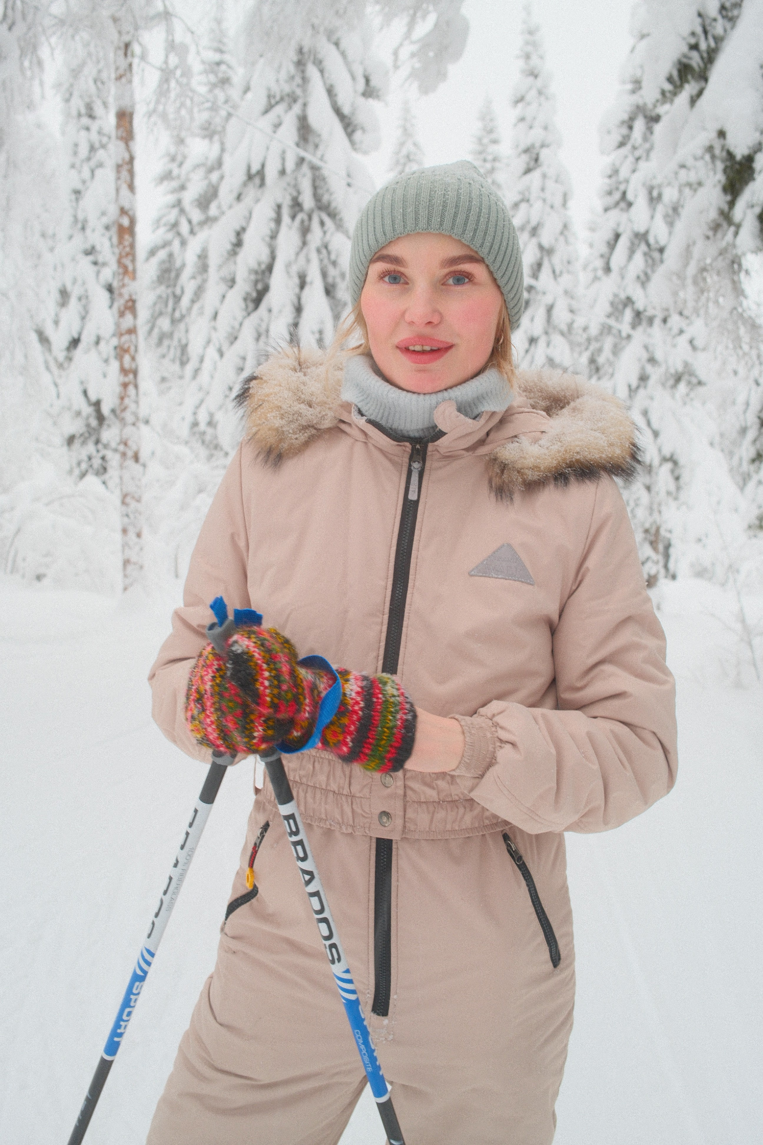 Девушка в бежевом лыжном костюме на лыжах в заснеженном зимнем лесу