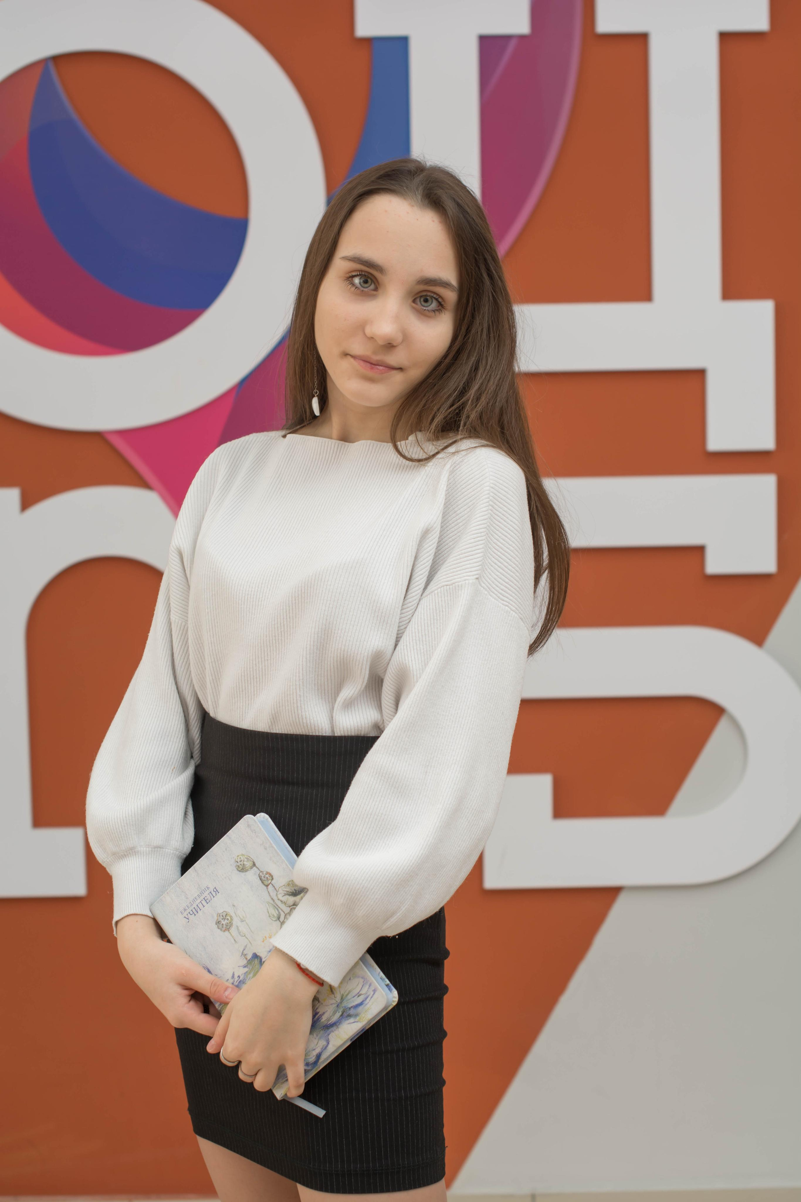 Красотка на фоне ОЦ 5 мило стоит с книгой в руках.