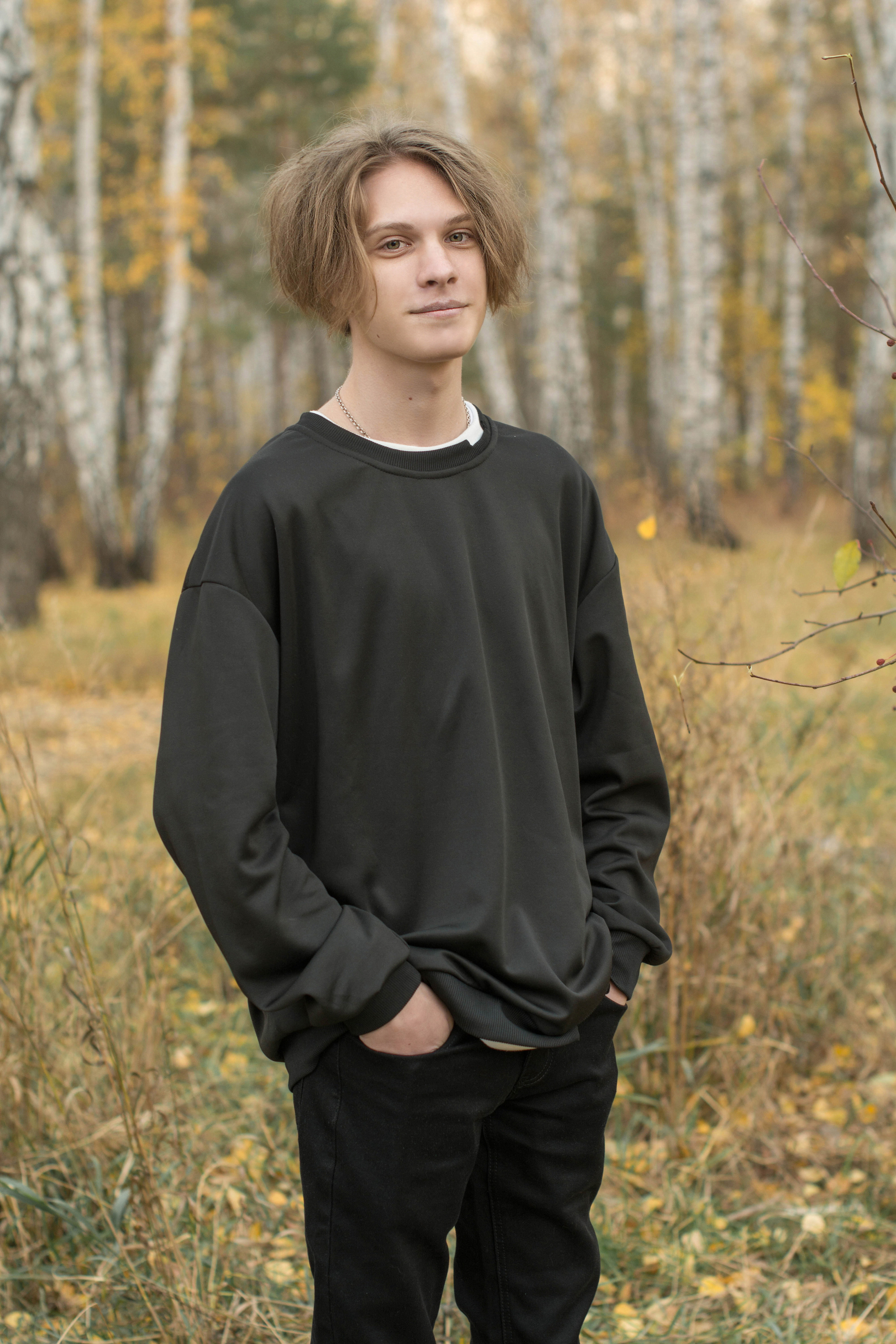 На фоне леса красиво стоит школьник в сером свитере.