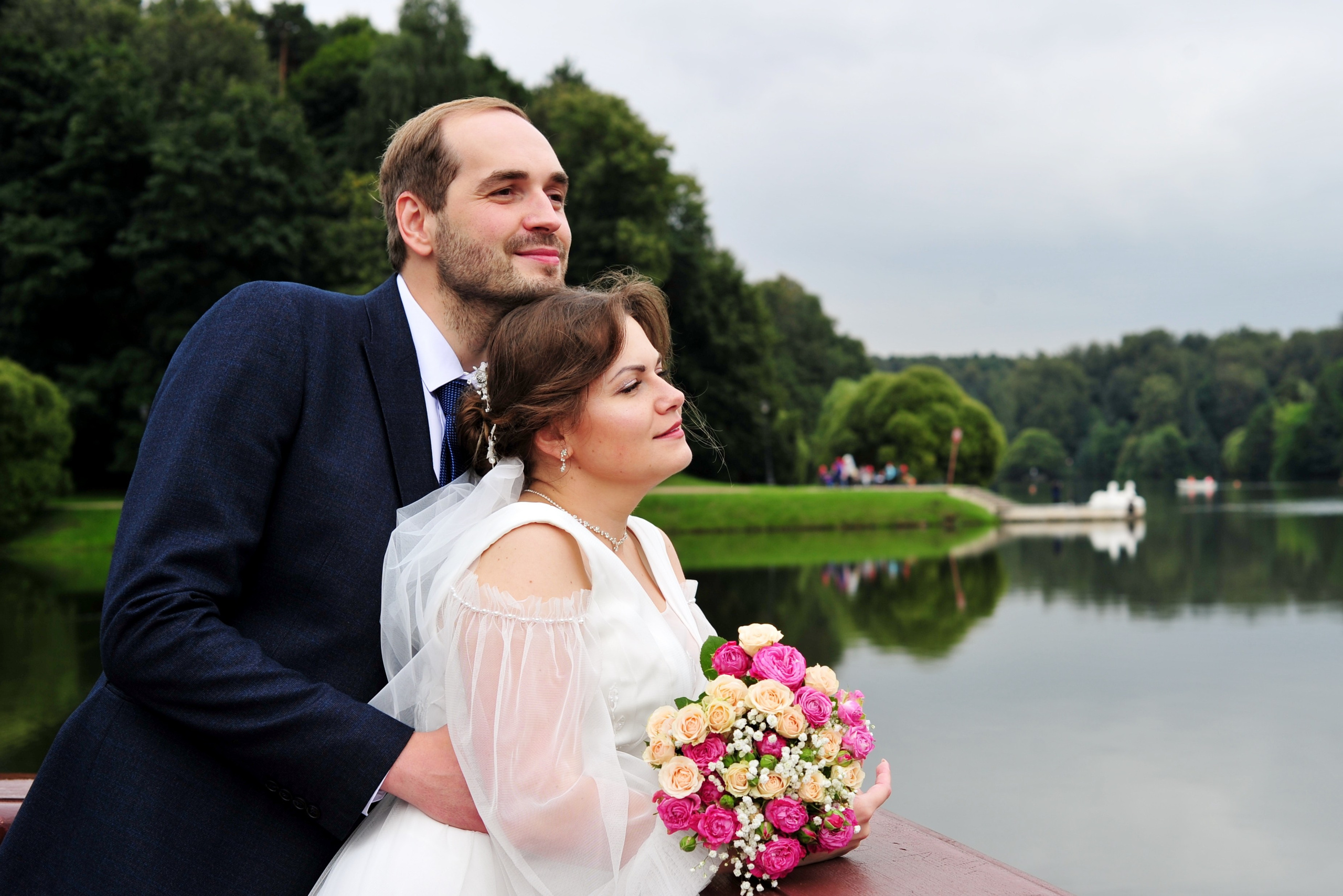 Свадьба в Царицыно пасмурным летним днем, молодожены стоят на берегу пруда и смотрят на воду 