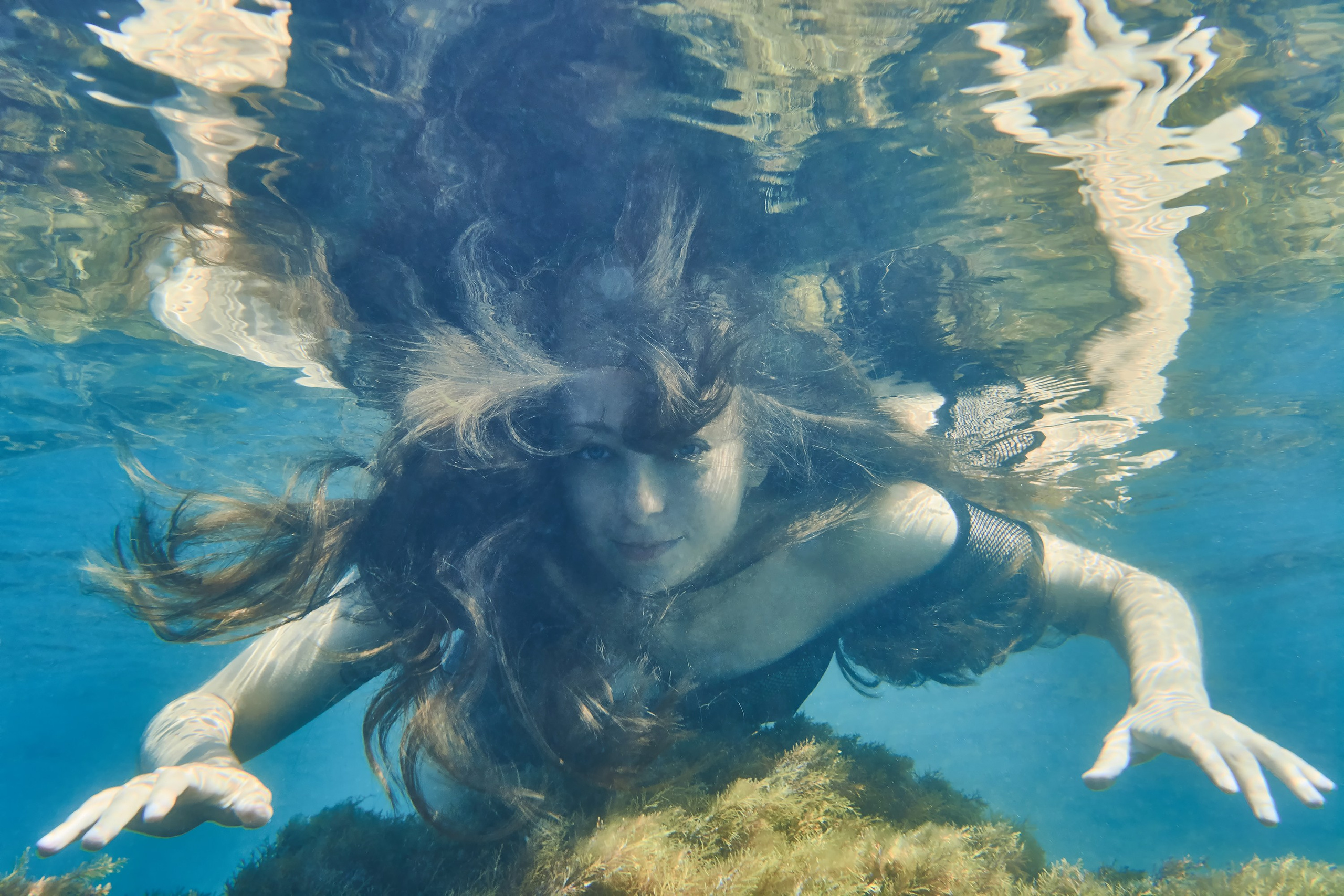 Девушка плывет под водой среди водорослей
