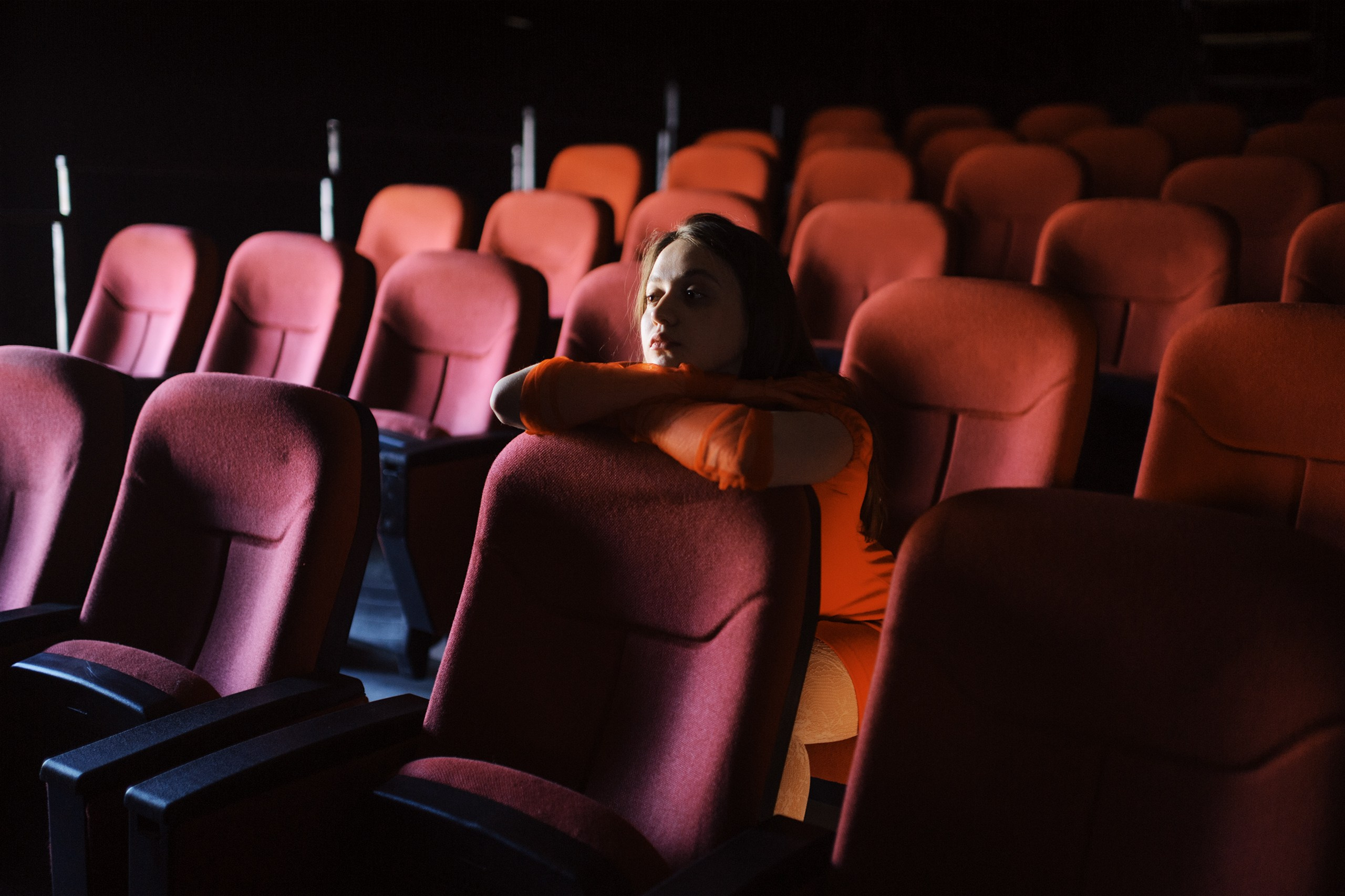 Девушка сидит на красных сидениях в кинозале