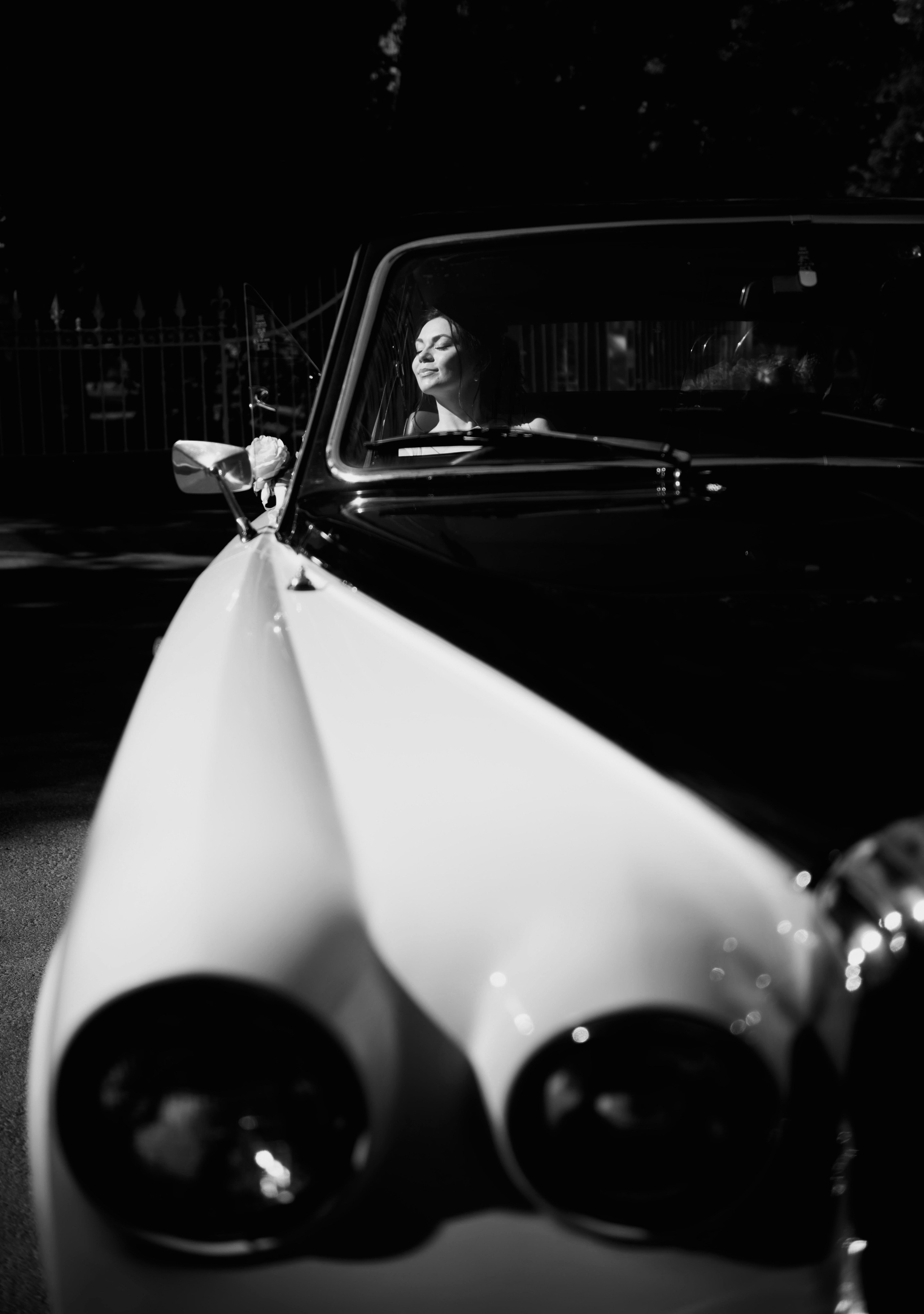 Портрет невесты, освещённой лучом солнца и сидящей в свадебной машине в черно-белых тонах.