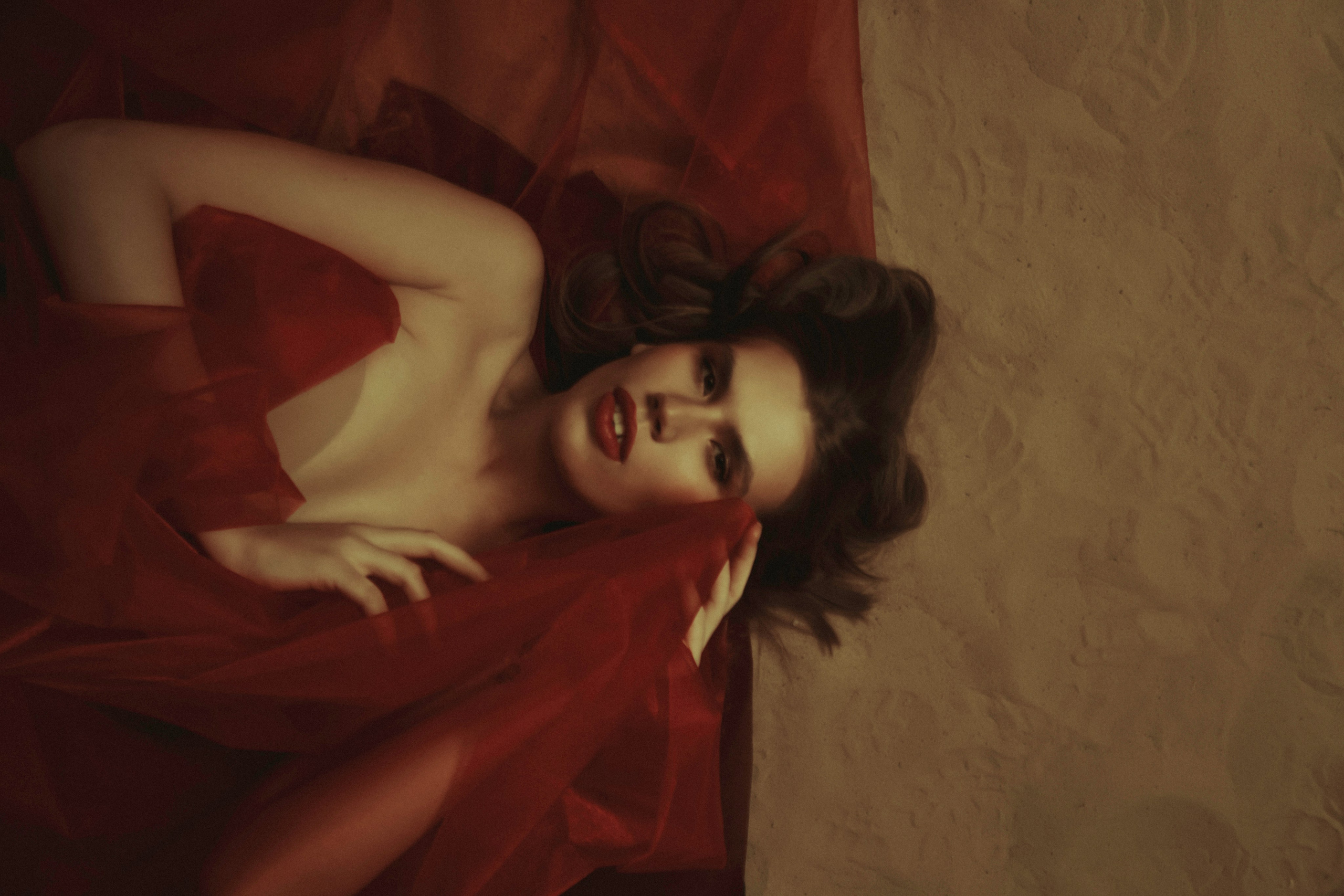 девушка лежит на песке в красной такни и укрывается ею показывая эмоции страсти в стиле картин Рубенса