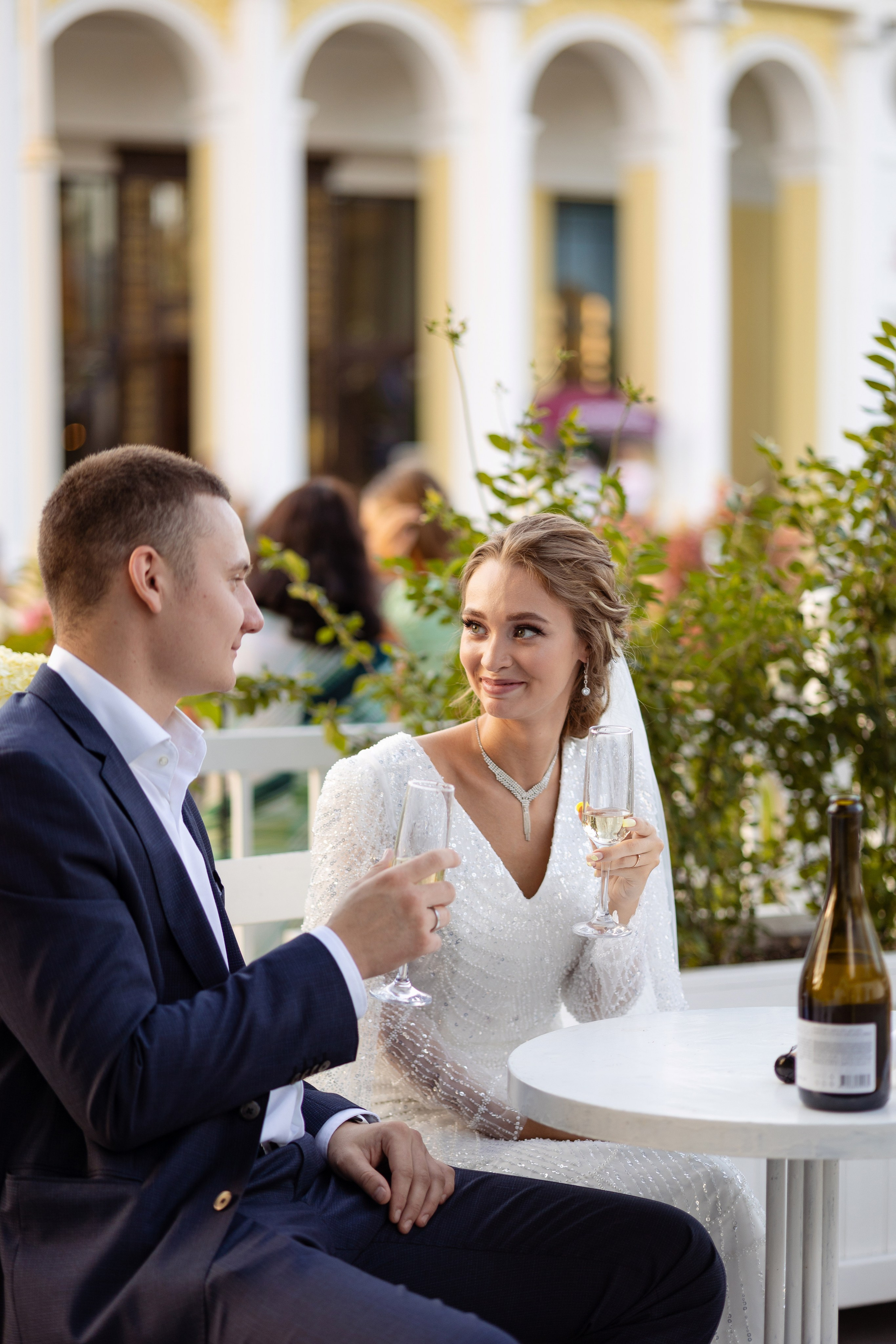 Молодые сидят за столом на фоне коллонады.