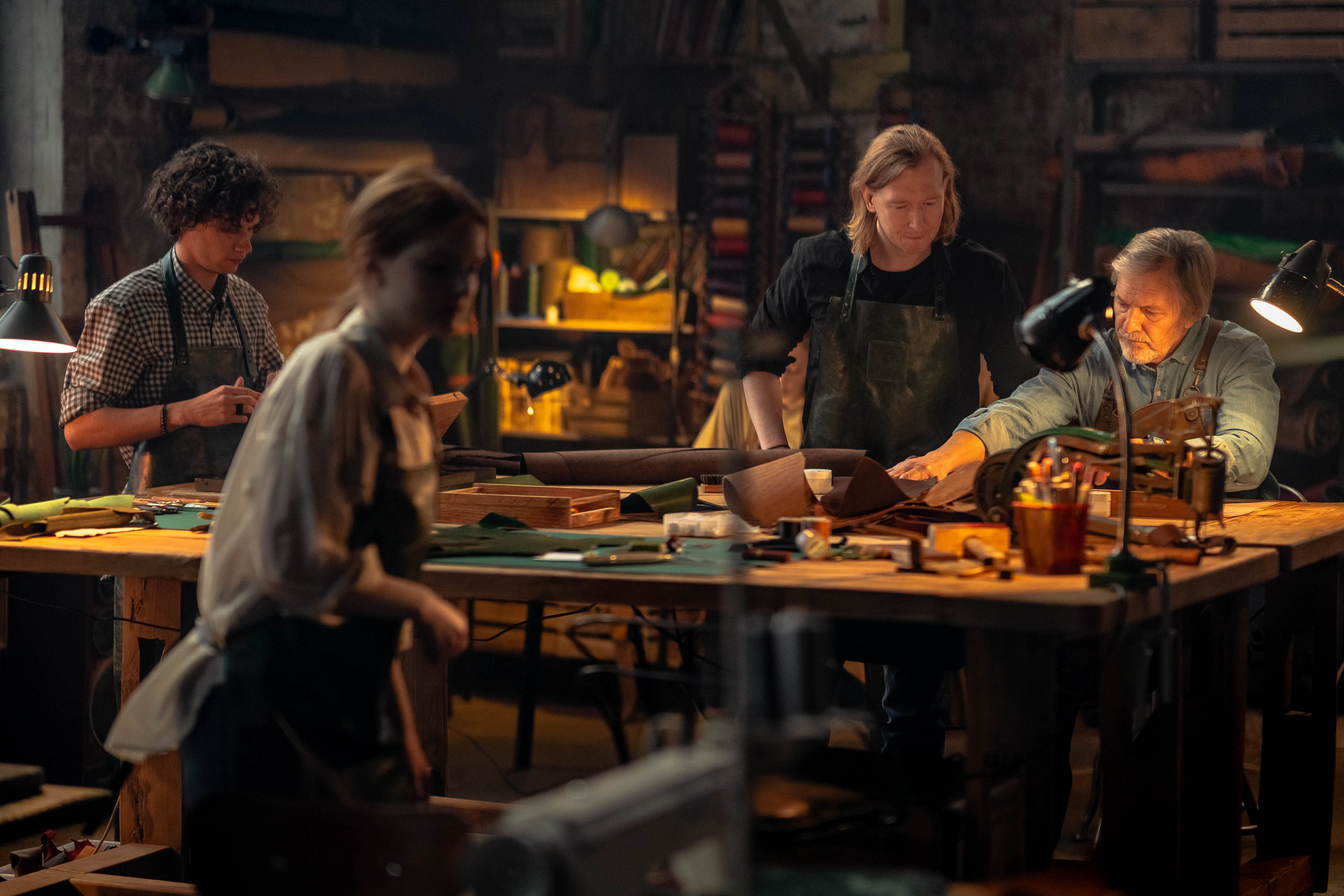 Приглушенный теплый свет в большом лофт-помещении с кирпичными стенами, команда кожевников работает за столом