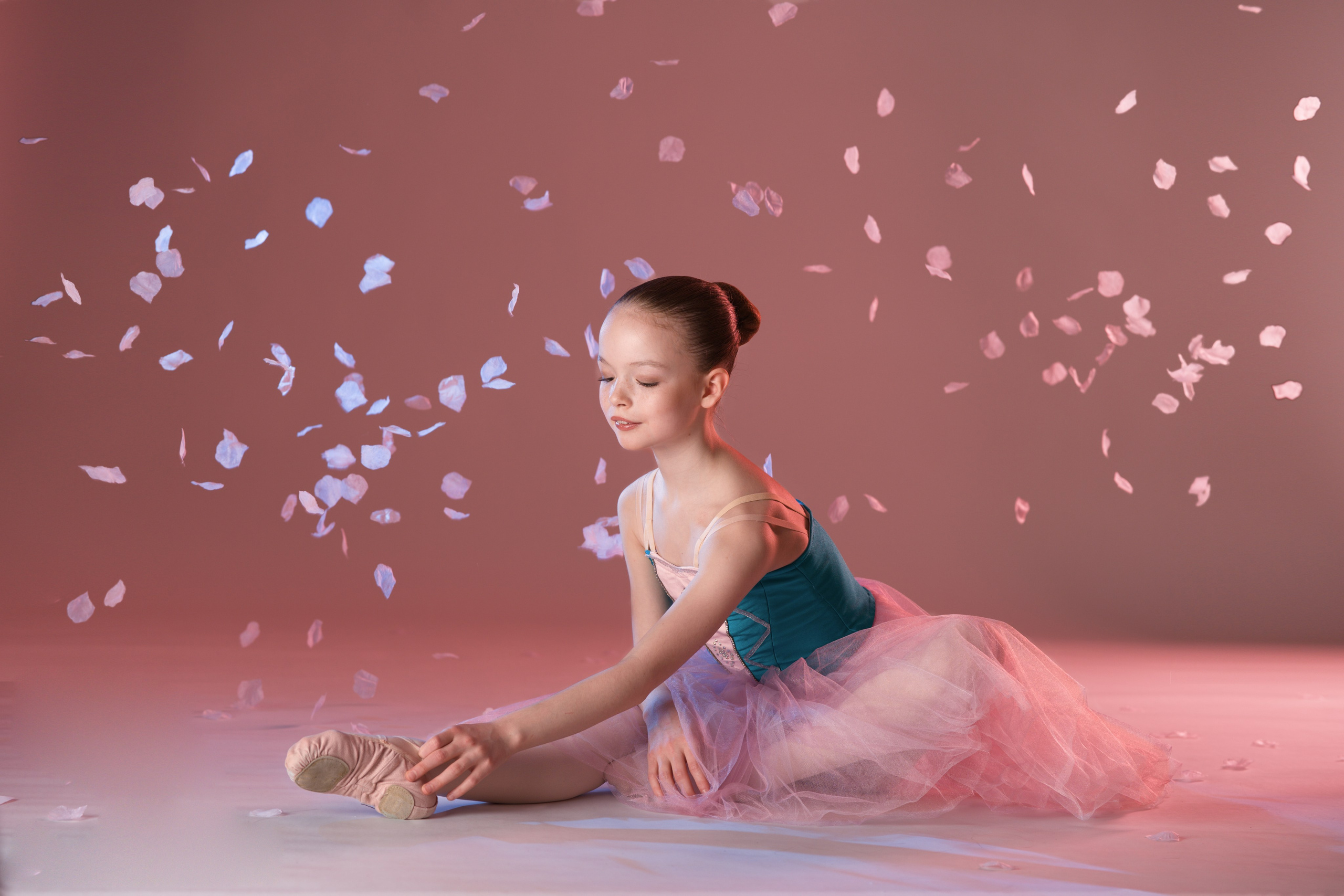 Портрет балерины на шпагате под дождем из лепестков. Статичная балетная поза, атмосфера нежности и легкости в стиле спорт-арт