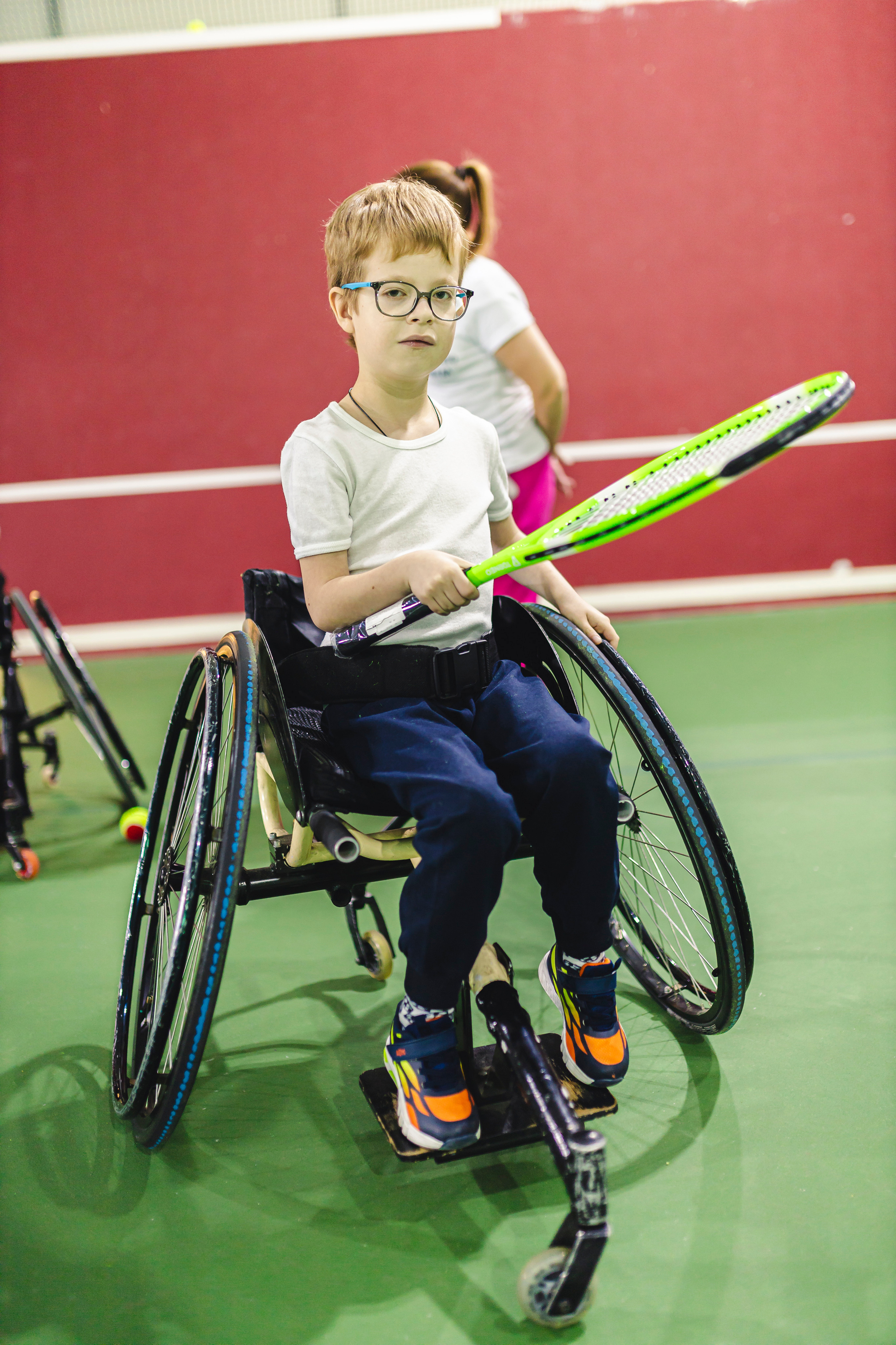 мальчик на коляске с теннисной ракеткой играет 