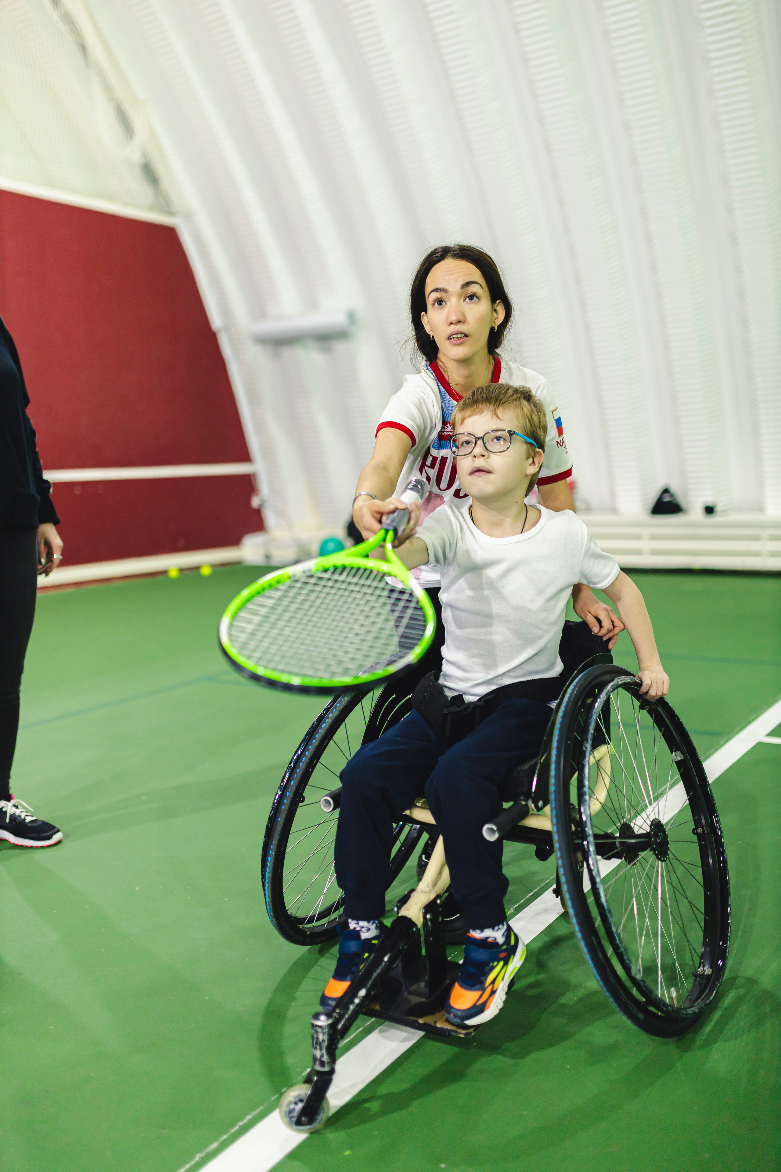 девушка учит мальчика на коляске играть в теннис 