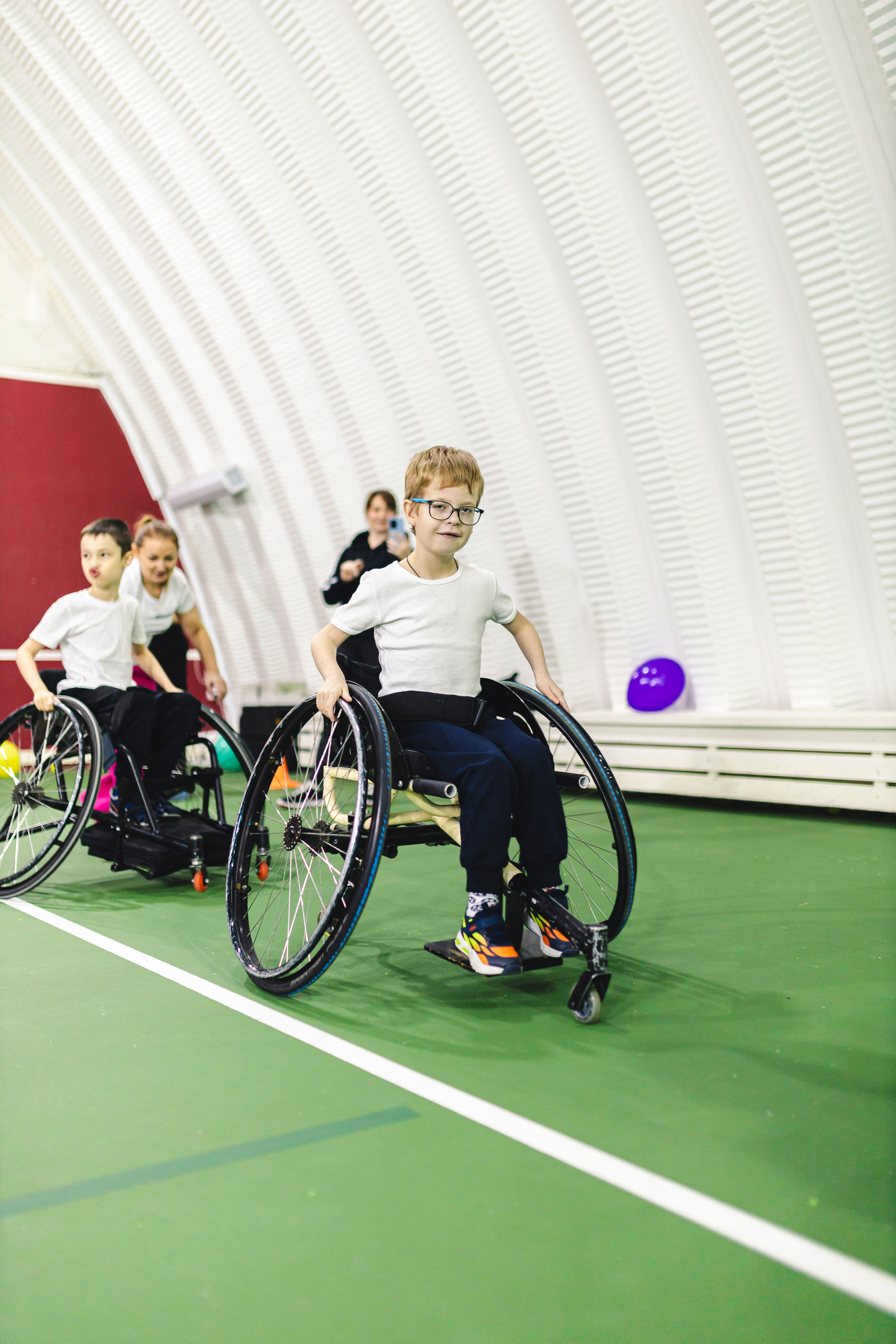 девочка на коляске в спорт зале играет в спортивные игры 