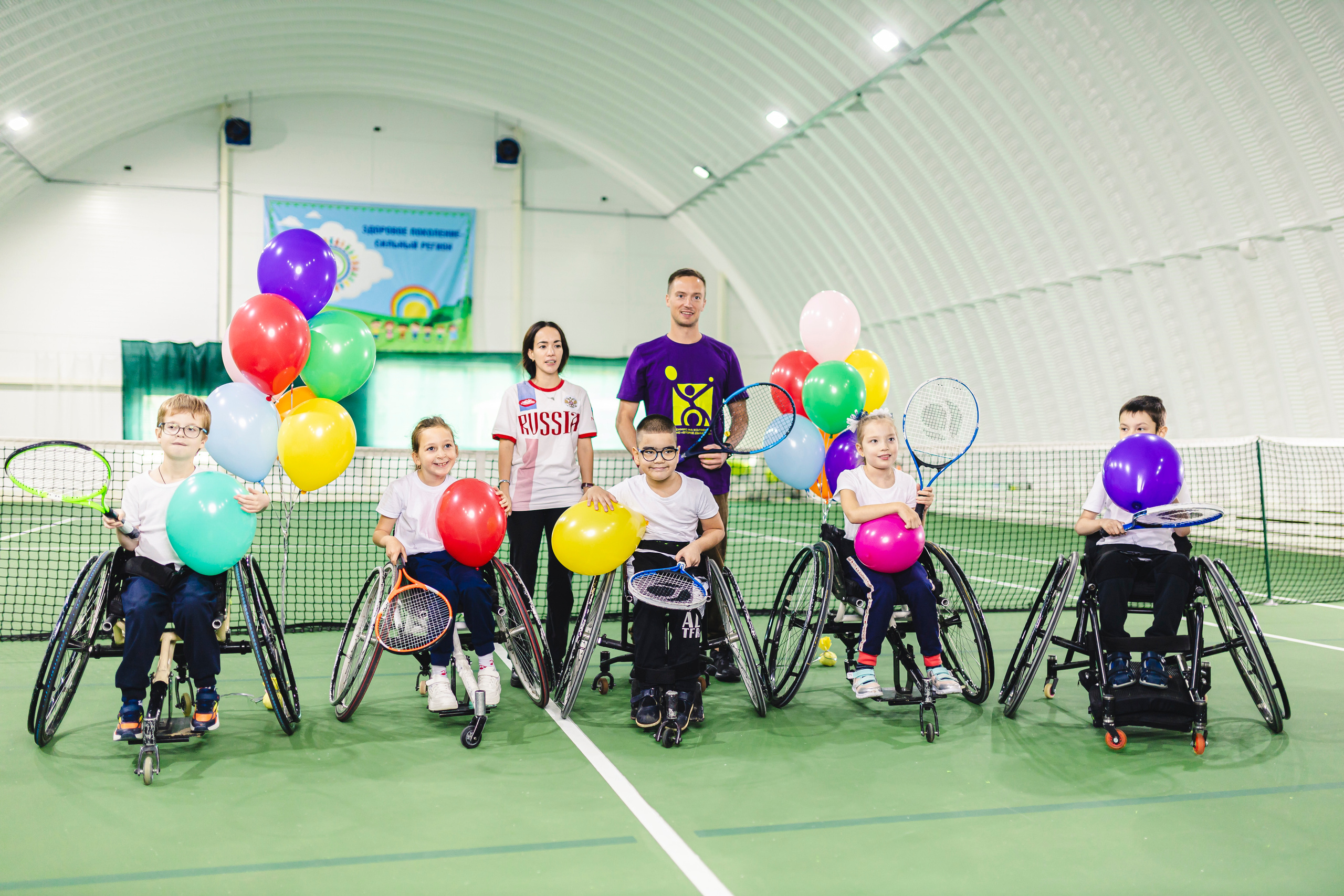 группа детей на колясках и воздушными шарами в спортивном зале 
